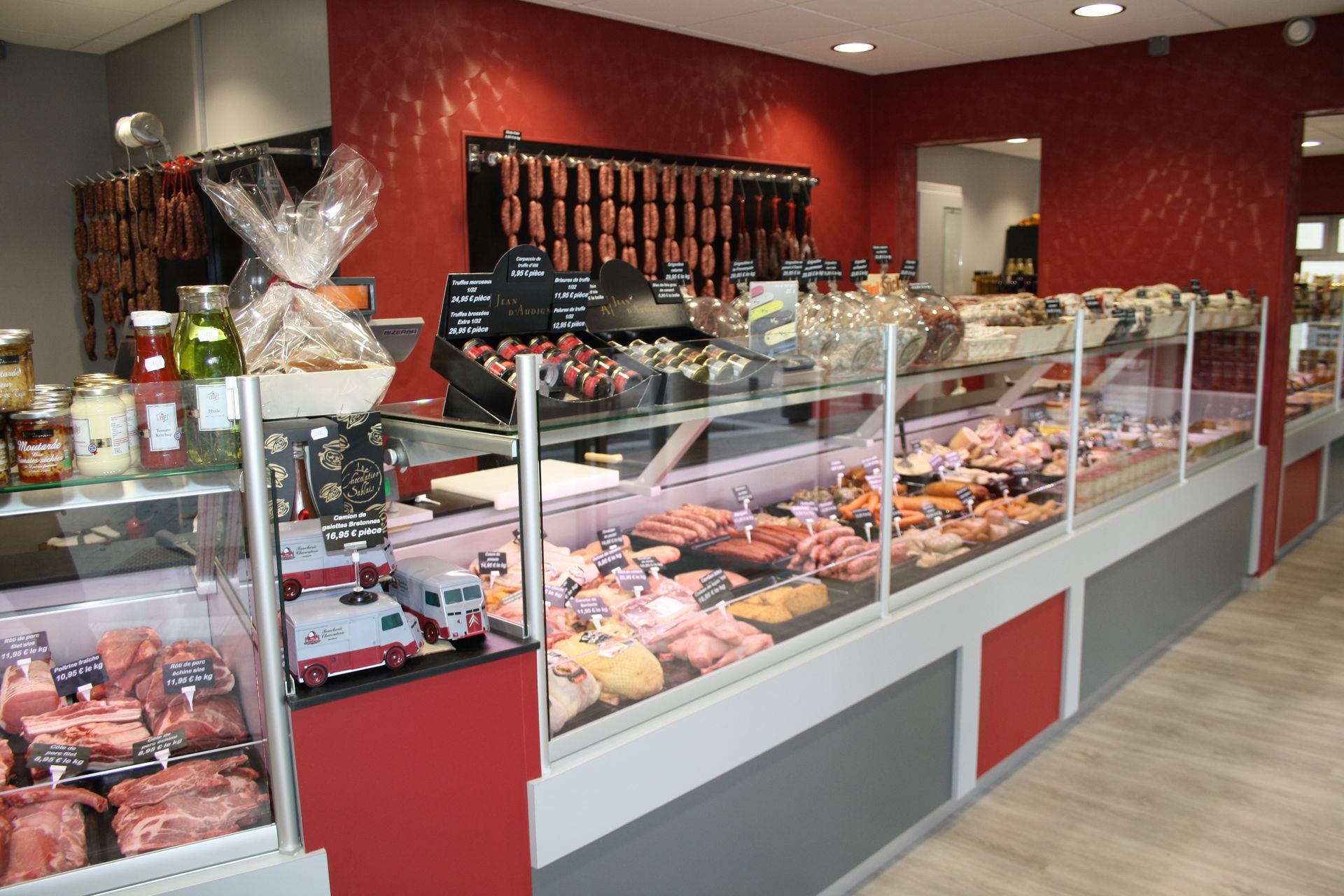 Présentoir de boucherie avec diverses viandes et saucisses. Touches de rouge et de gris.