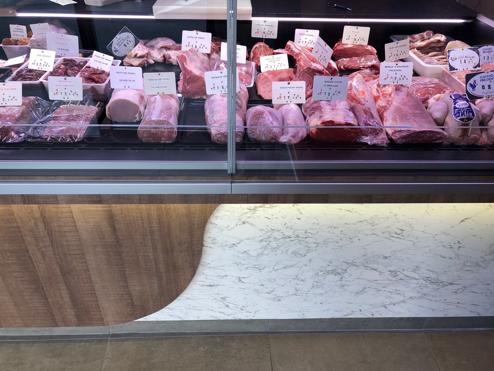 Vitrine à viande présentant différentes coupes, étiquettes de prix blanches. Surfaces en bois et texturées.