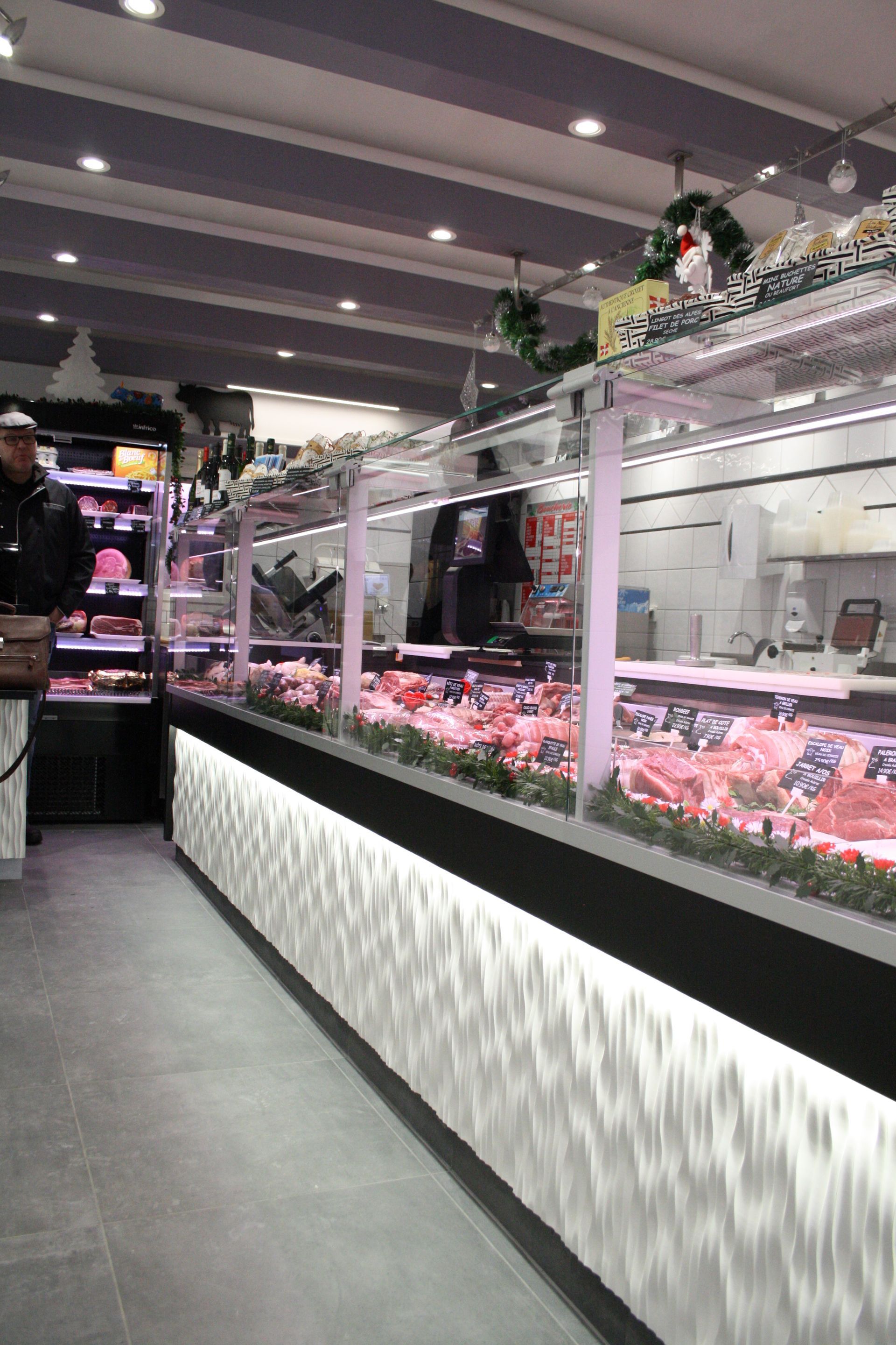 Dans une boucherie, une longue vitrine remplie de viande, avec une façade à motifs et un éclairage vif au plafond.