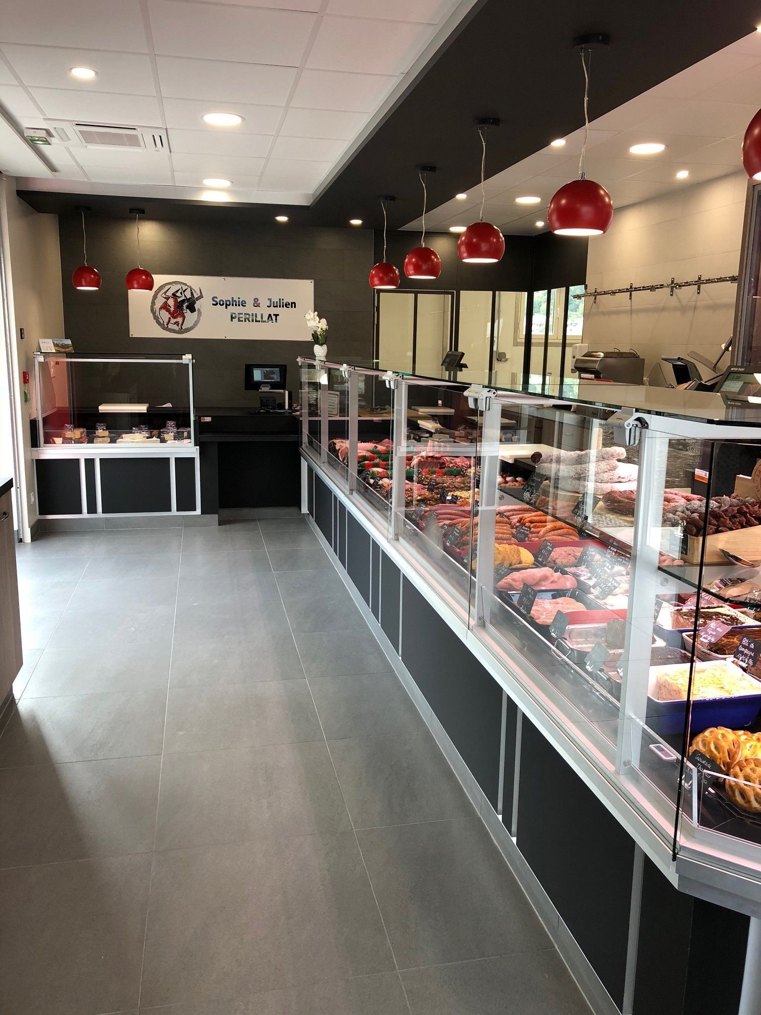 Intérieur d'une boucherie avec vitrines de viandes, éclairage rouge au plafond et sol gris.