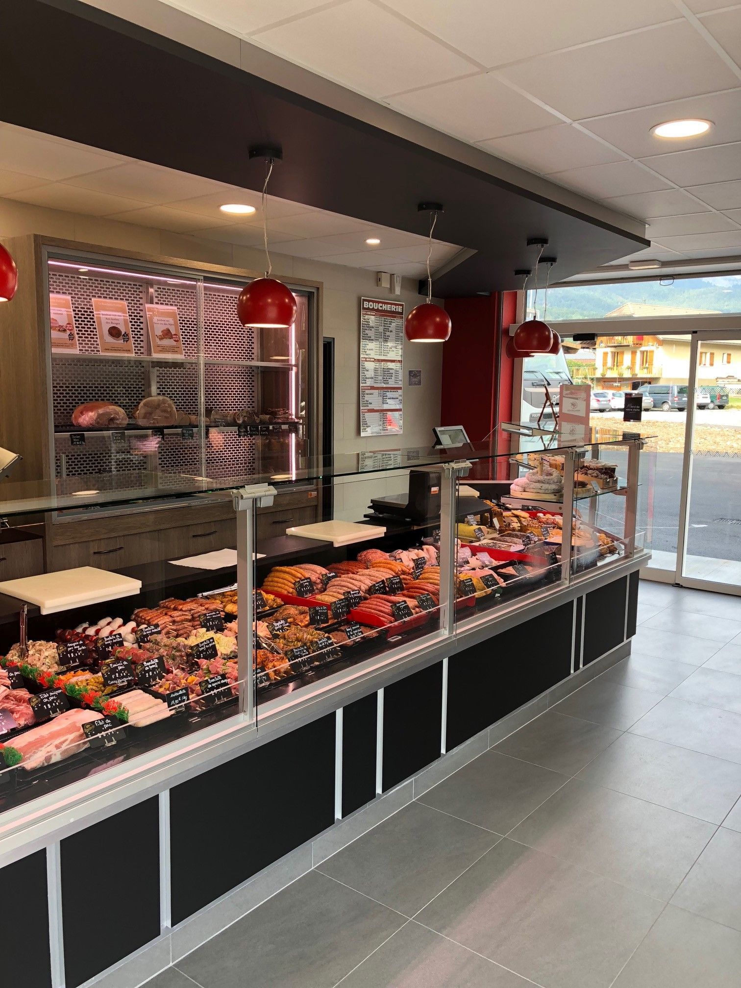 Intérieur d'une boucherie : vitrine présentant des produits carnés ; suspensions lumineuses rouges ; porte vitrée.