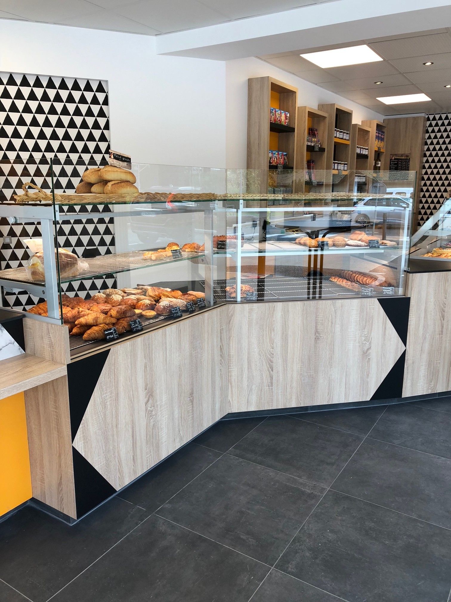 Vitrine de boulangerie avec pâtisseries, vitrines en verre, éléments en bois et noirs, et décoration murale géométrique.
