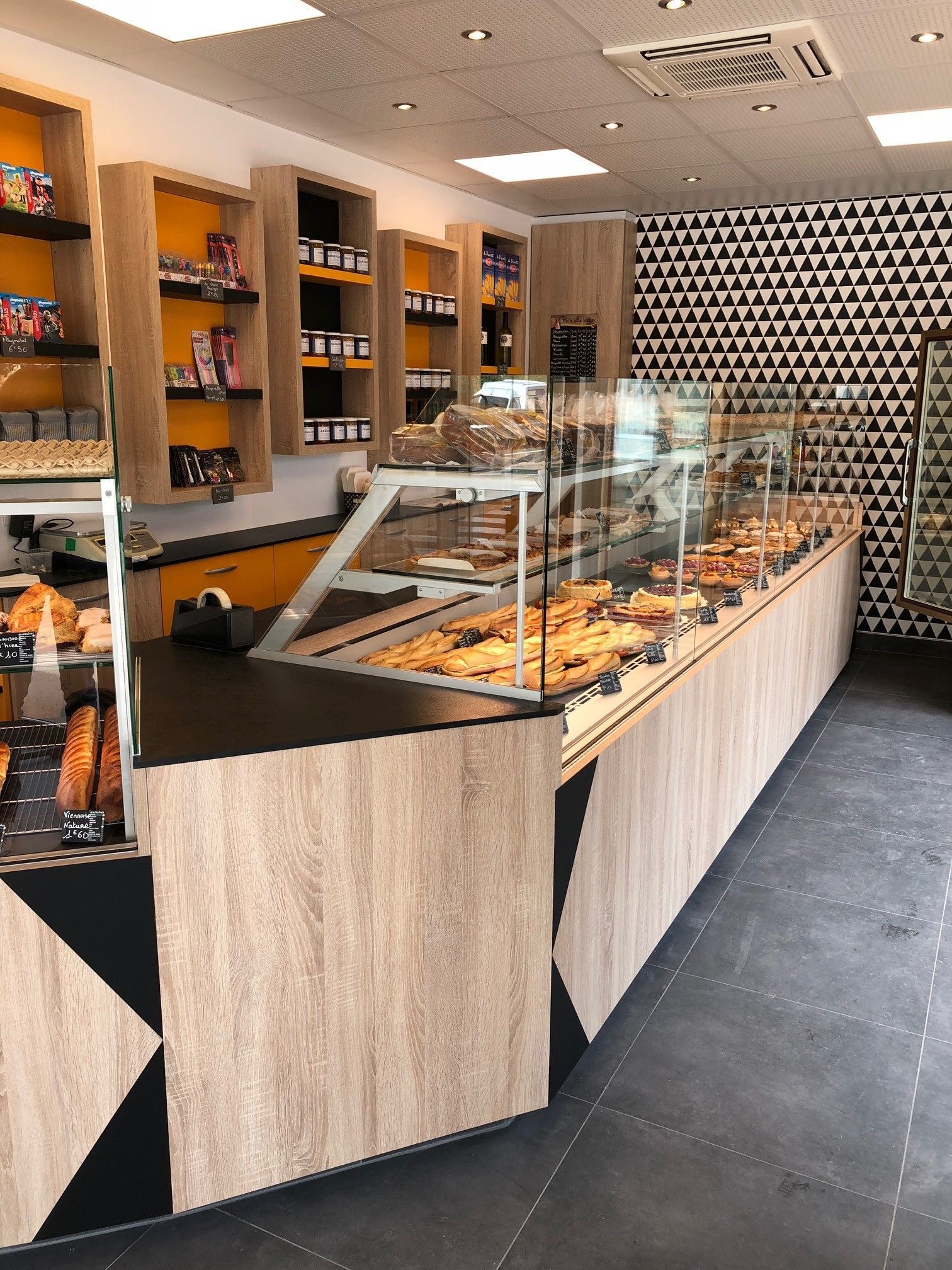 Intérieur de boulangerie avec des produits de boulangerie présentés dans des vitrines ; accents de bois et de noir.