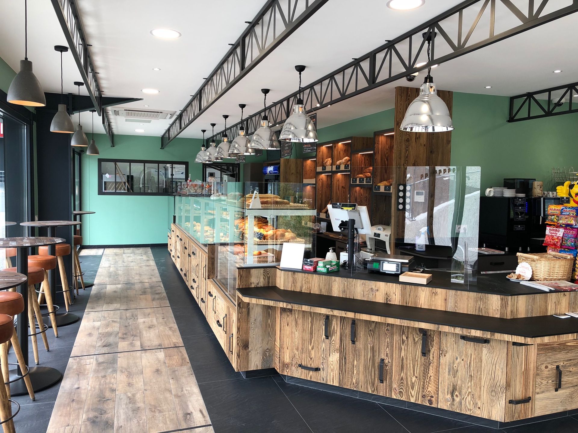 Intérieur d'une boulangerie avec un comptoir présentant des pâtisseries, des éléments en bois et des suspensions lumineuses.