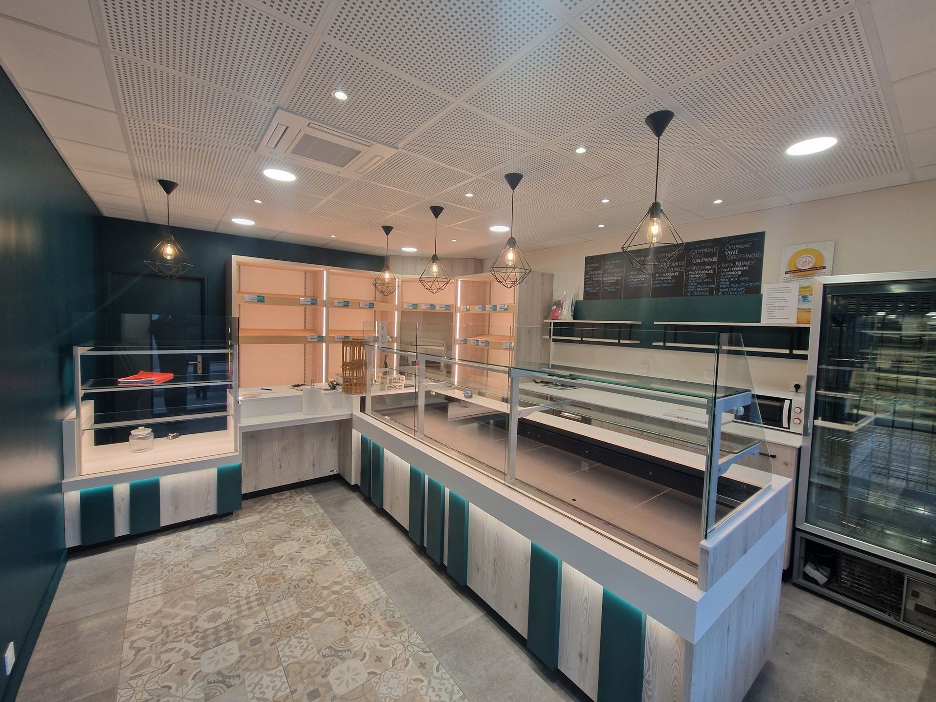 Intérieur d'une boulangerie vide avec comptoirs d'exposition, touches turquoise et plafond décoratif.