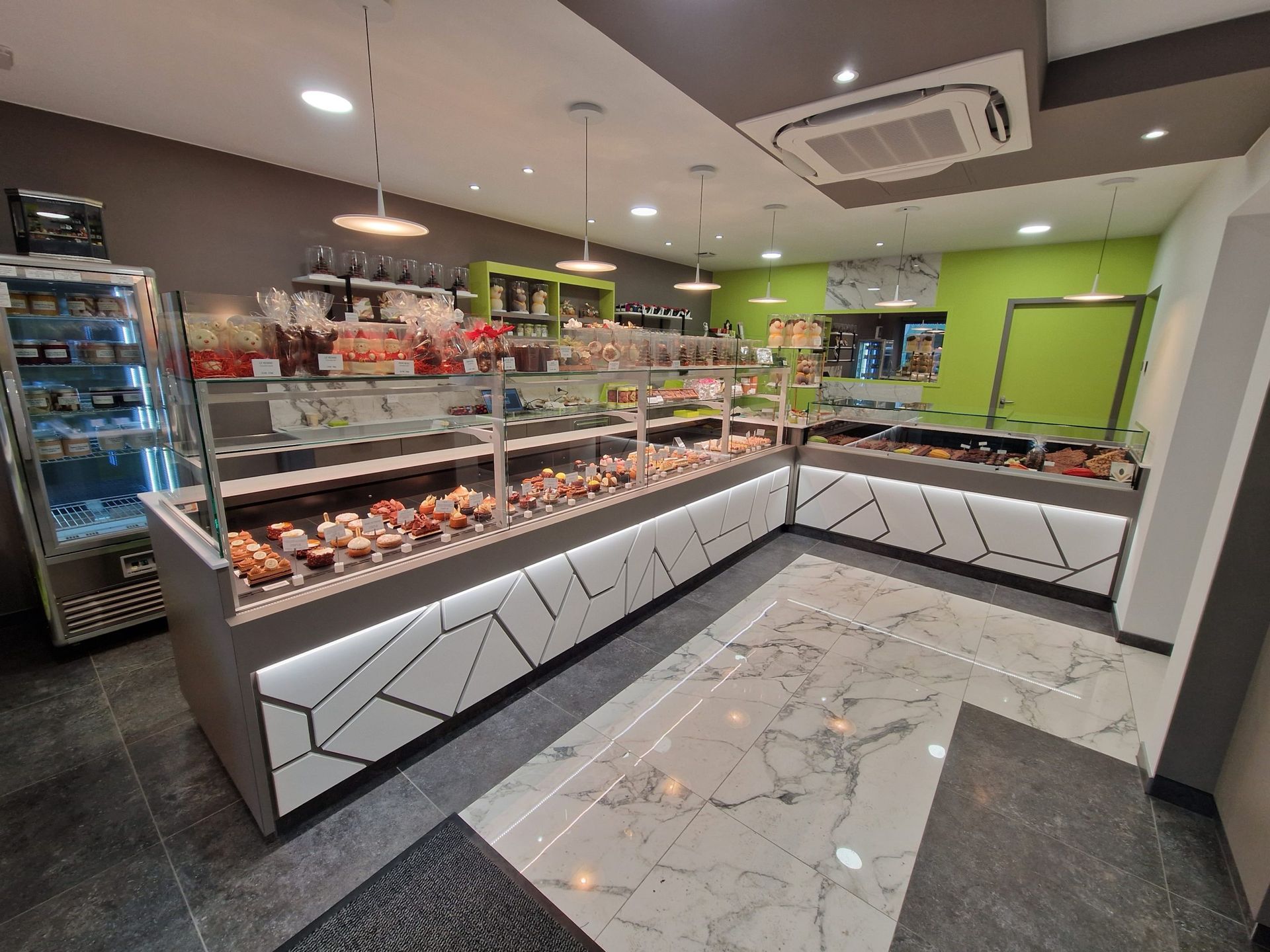Intérieur d'une pâtisserie avec vitrines remplies de pâtisseries, design moderne avec des touches de gris et de blanc.