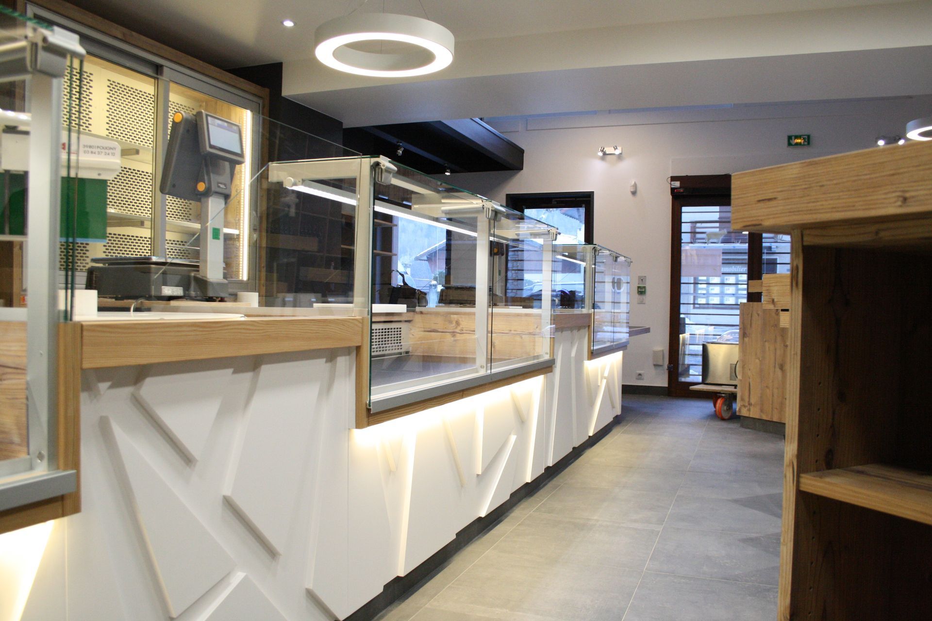 L'intérieur d'une boulangerie moderne avec des vitrines, un comptoir au design géométrique et un éclairage encastré.