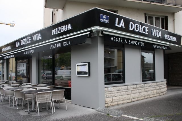 Extérieur du restaurant La Dolce Vita Pizzeria avec auvent, terrasse et façade grise moderne.