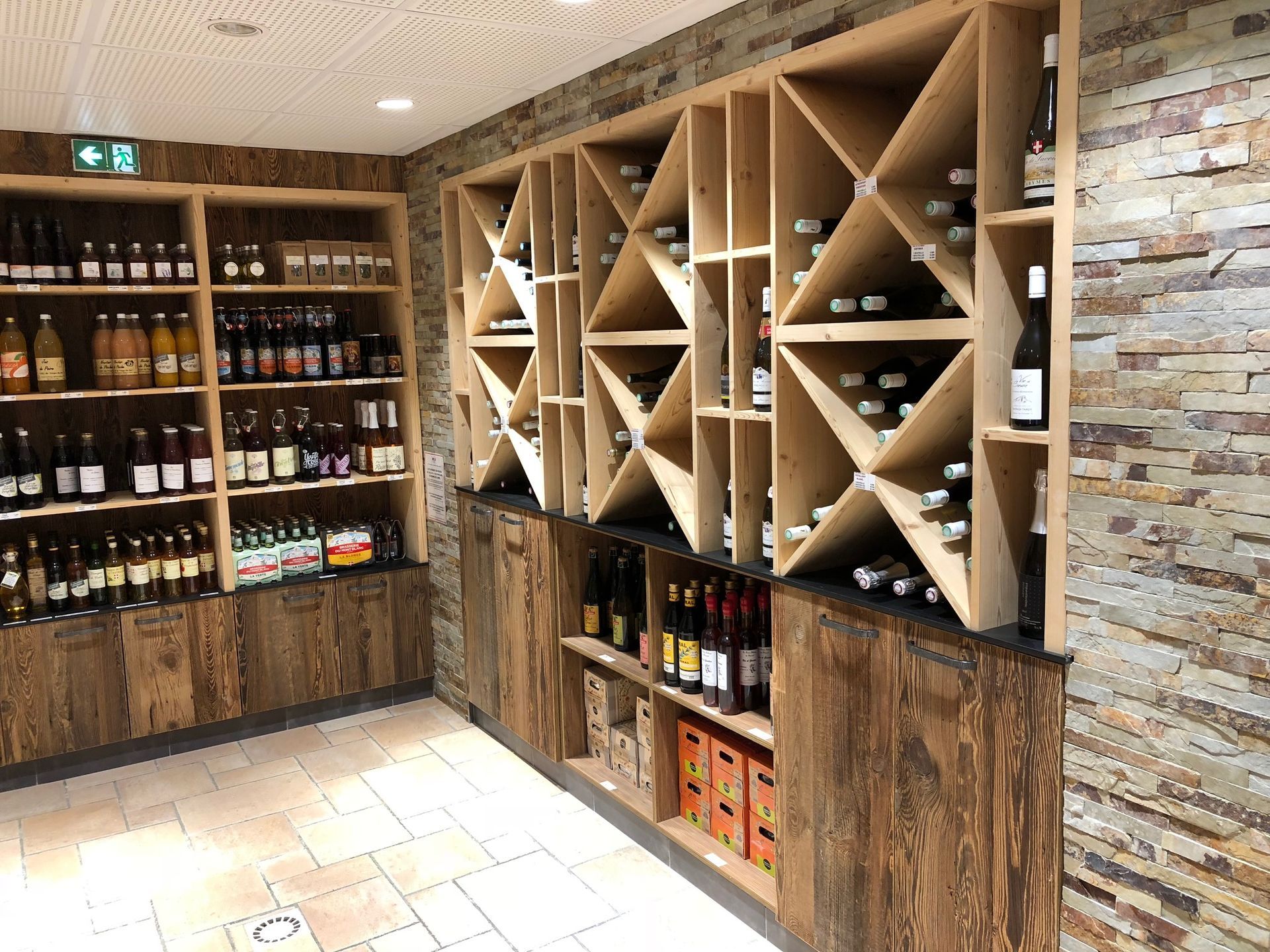 Présentoir à vins et boissons dans un magasin, avec étagères en bois et mur en pierre, les bouteilles étant disposées pour la vente.