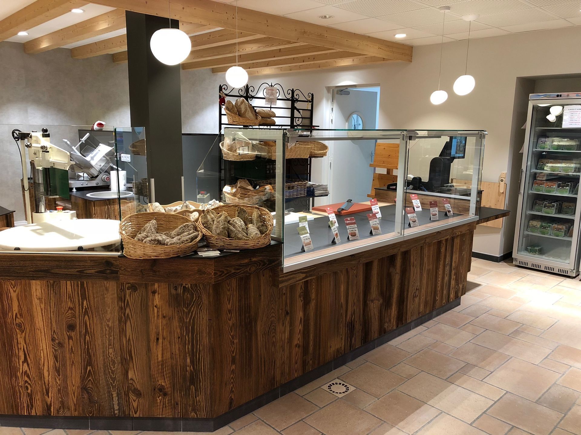 Intérieur de la boulangerie : comptoir en bois présentant le pain et les plats préparés, avec une vitrine réfrigérée.