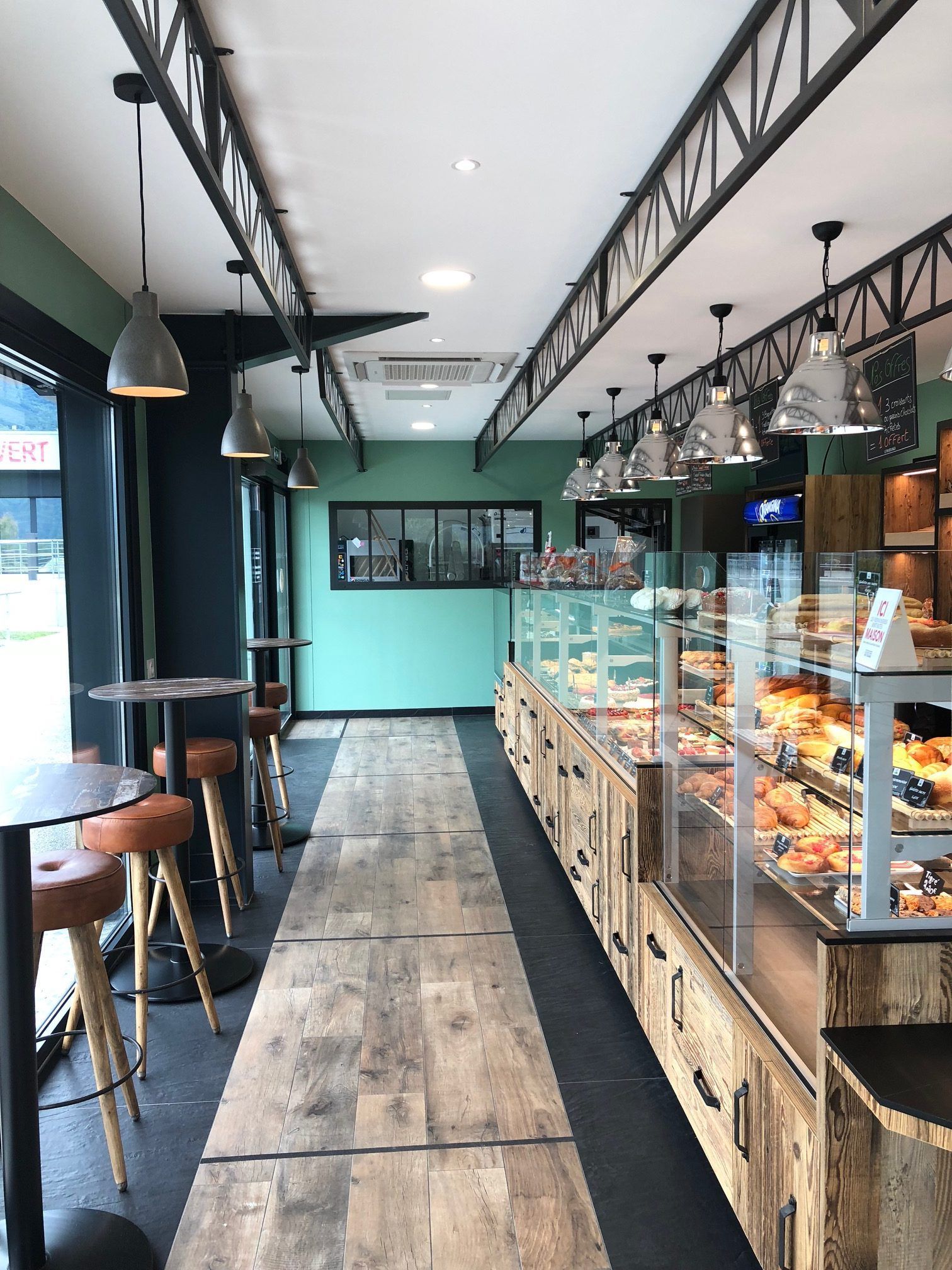 Intérieur de boulangerie avec vitrine à pâtisseries, parquet et sièges.