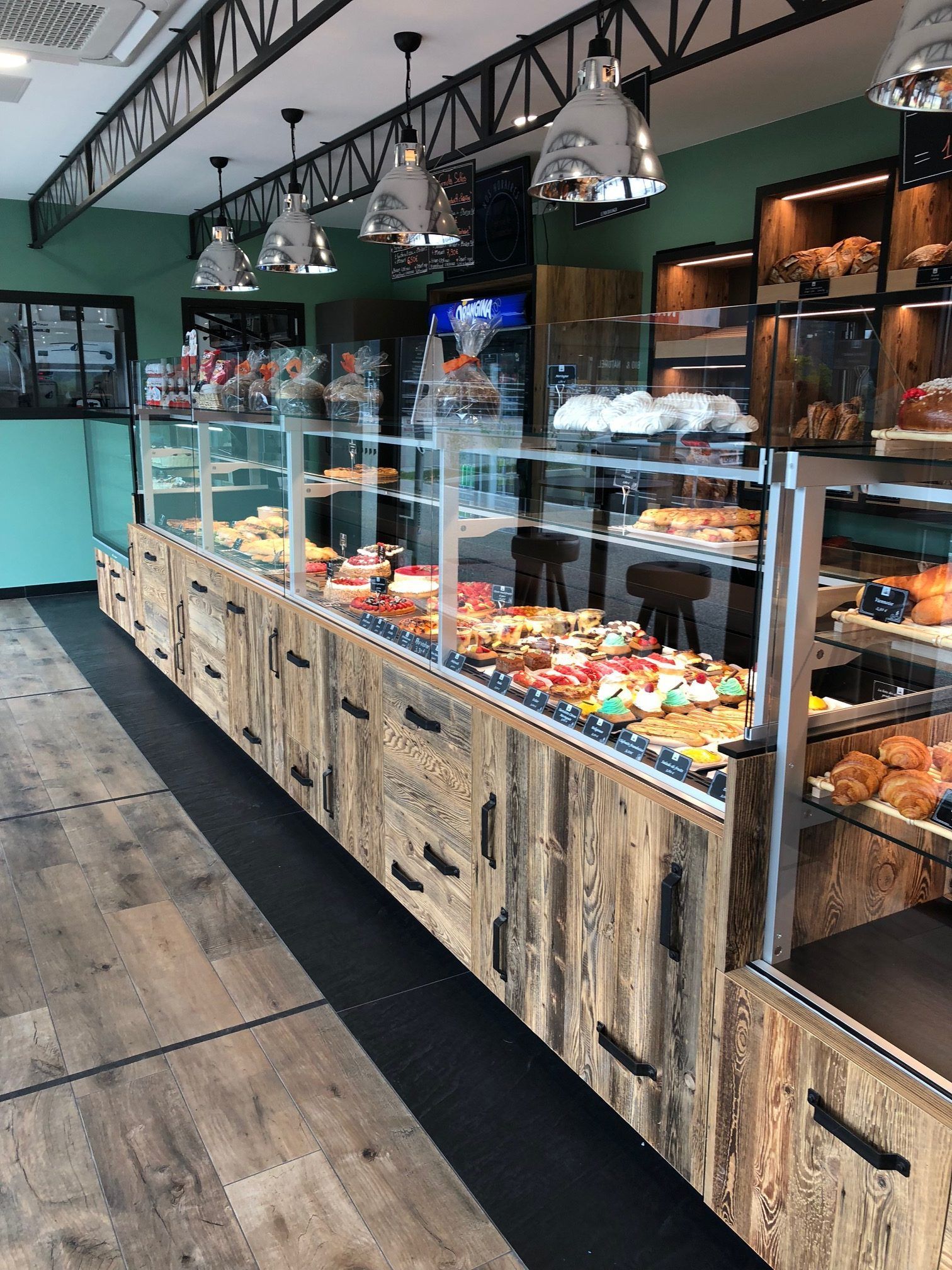 Intérieur de boulangerie avec une longue vitrine remplie de pâtisseries et de viennoiseries. Murs rustiques en bois et bleu turquoise.