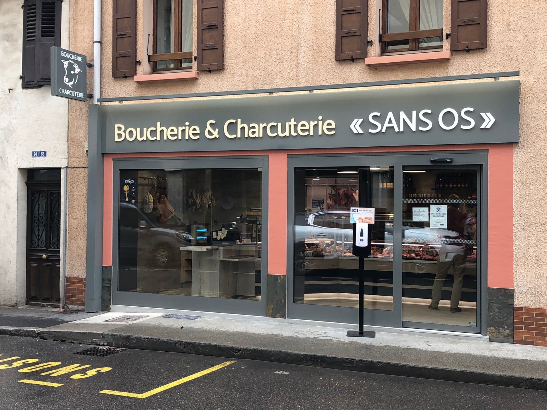 Boucherie « SANS OS » avec de grandes fenêtres, une façade grise et des finitions roses.