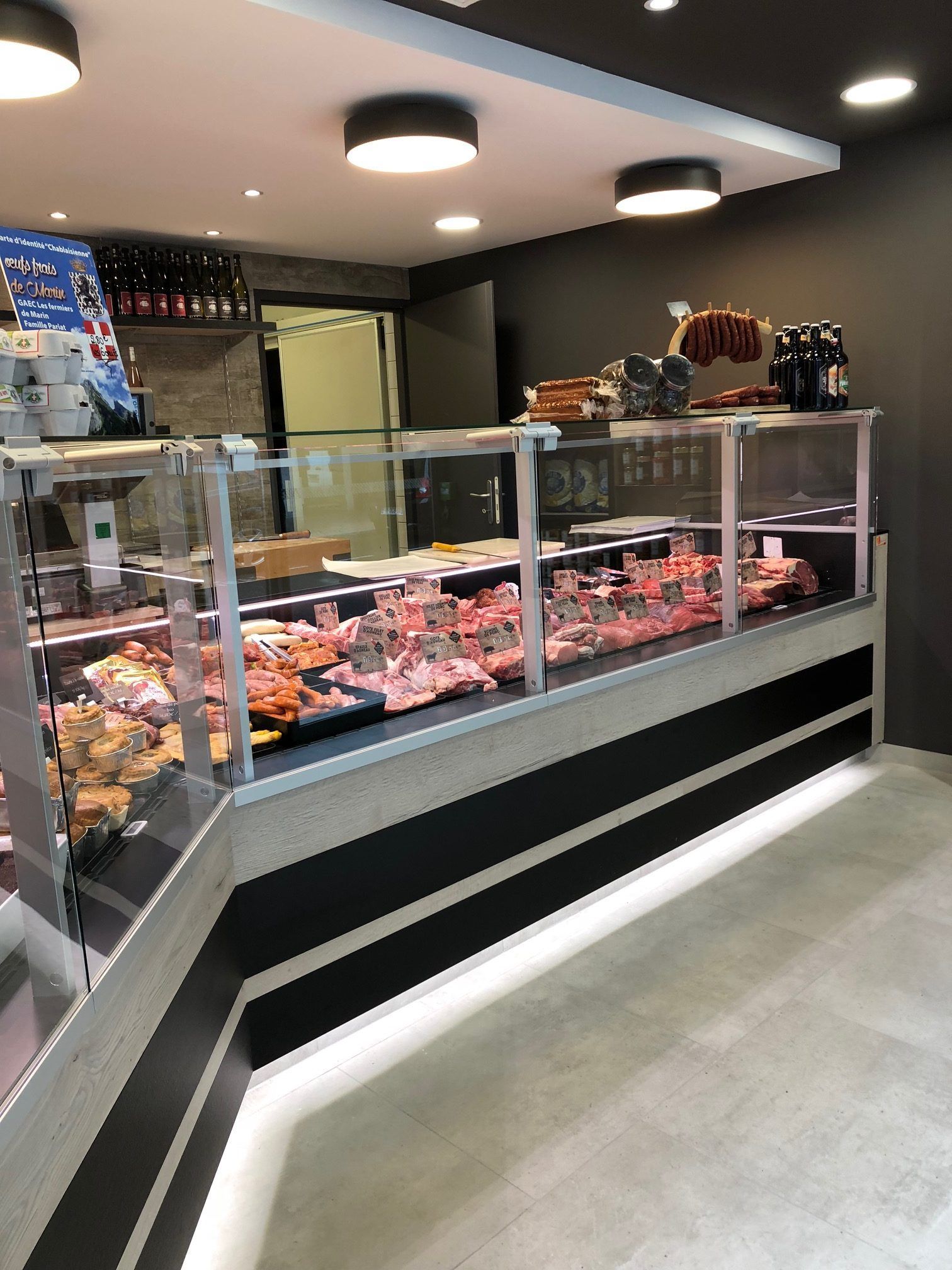 Vitrine de boucherie présentant différentes coupes de viande. Intérieur aux accents gris et noirs.
