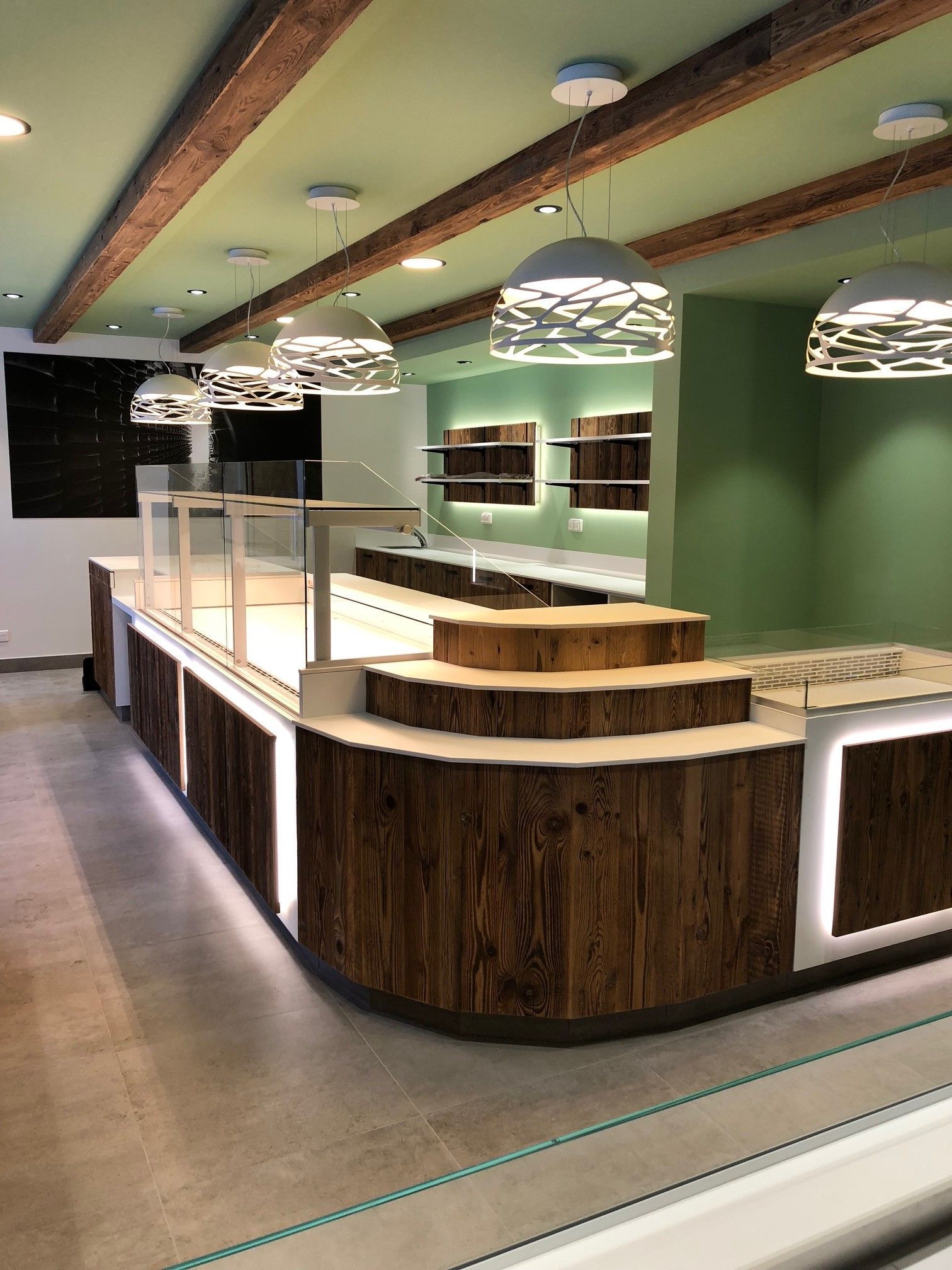 Une boulangerie avec un comptoir et des étagères en bois, des murs verts et des suspensions lumineuses décoratives.