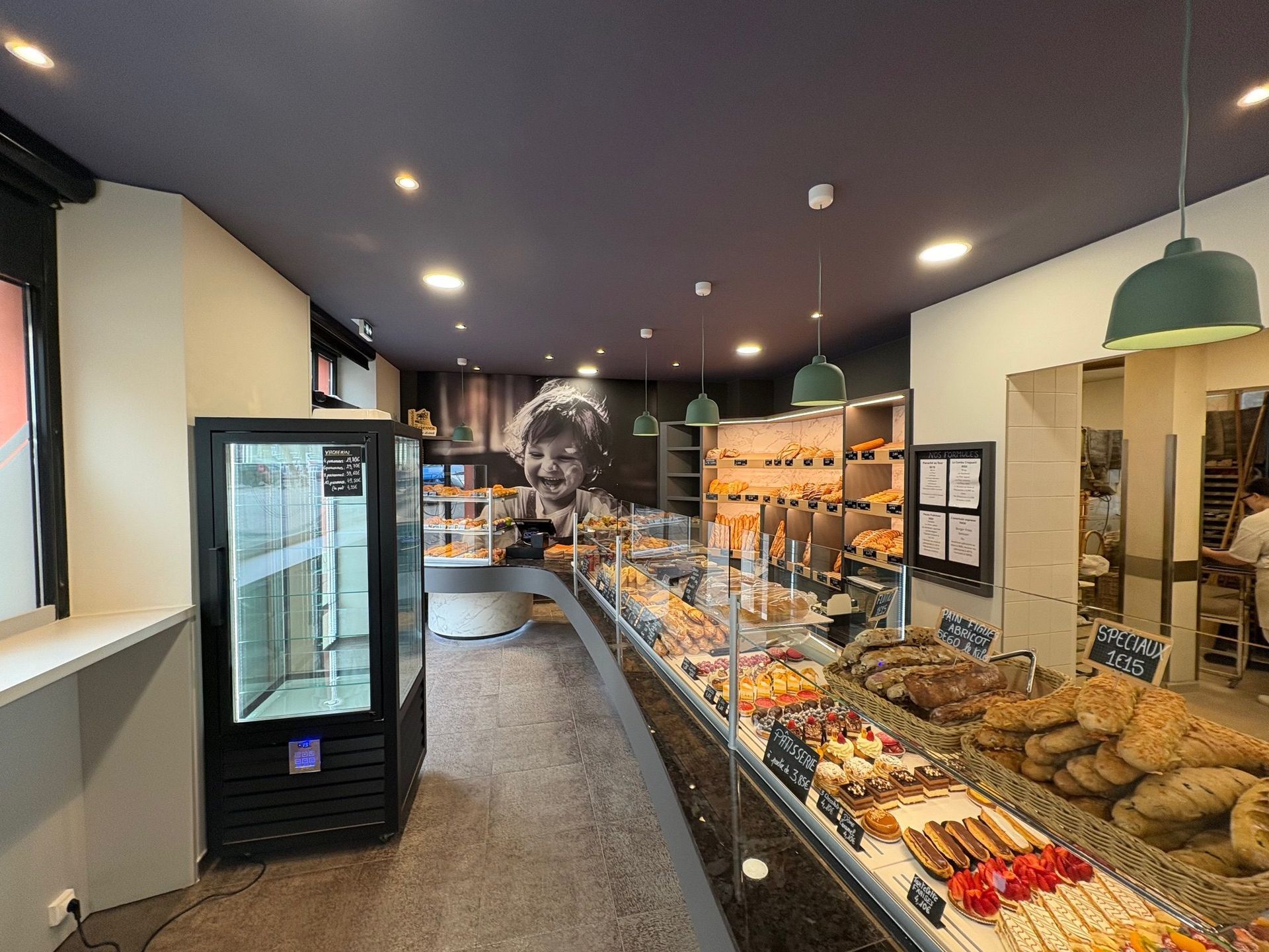 Intérieur d'une boulangerie avec des pâtisseries exposées dans des vitrines. Un portrait d'enfant est accroché au mur.