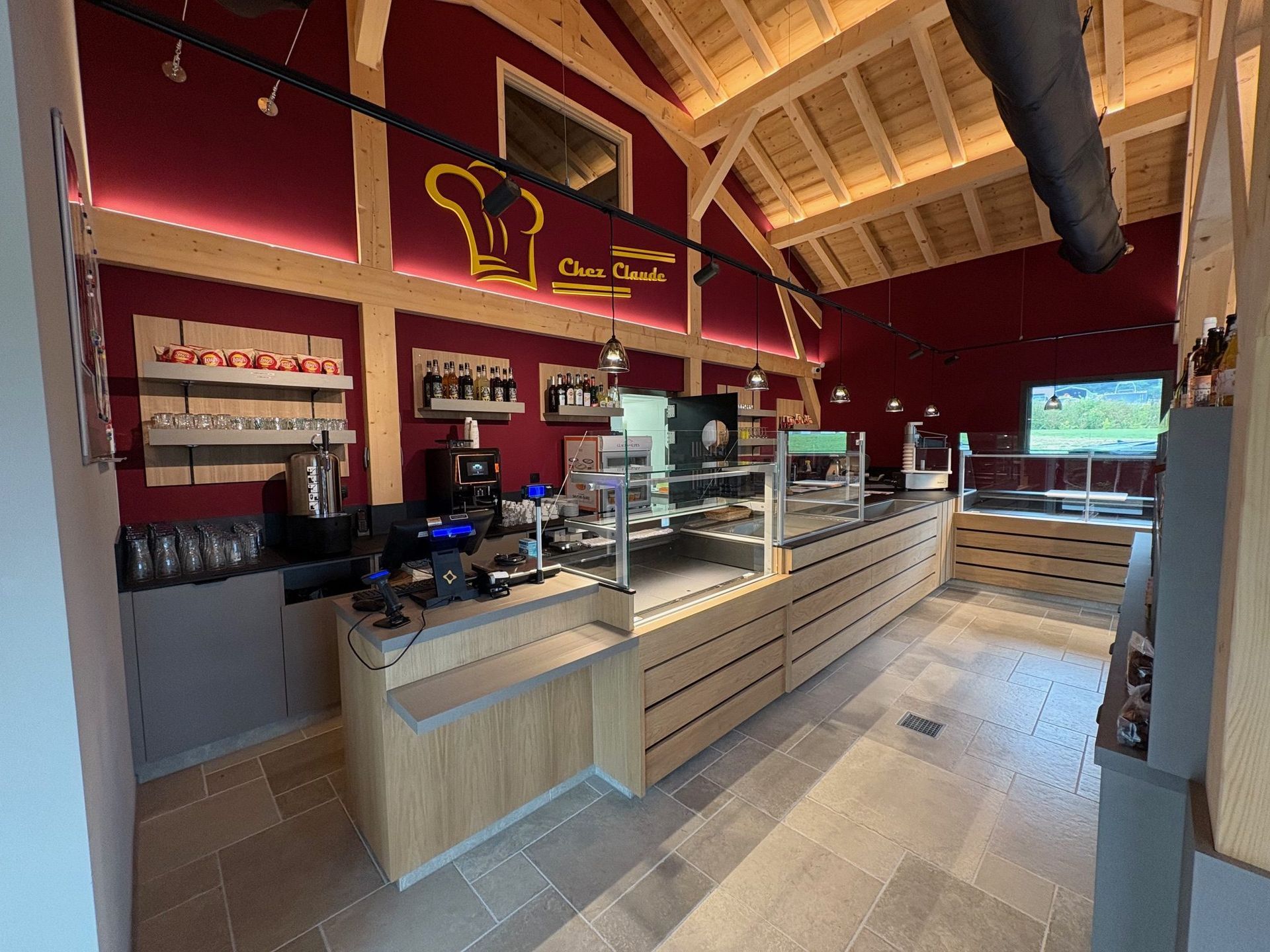 Intérieur d'une boulangerie avec un comptoir, des vitrines et des murs rouges. On aperçoit des poutres et des étagères en bois.