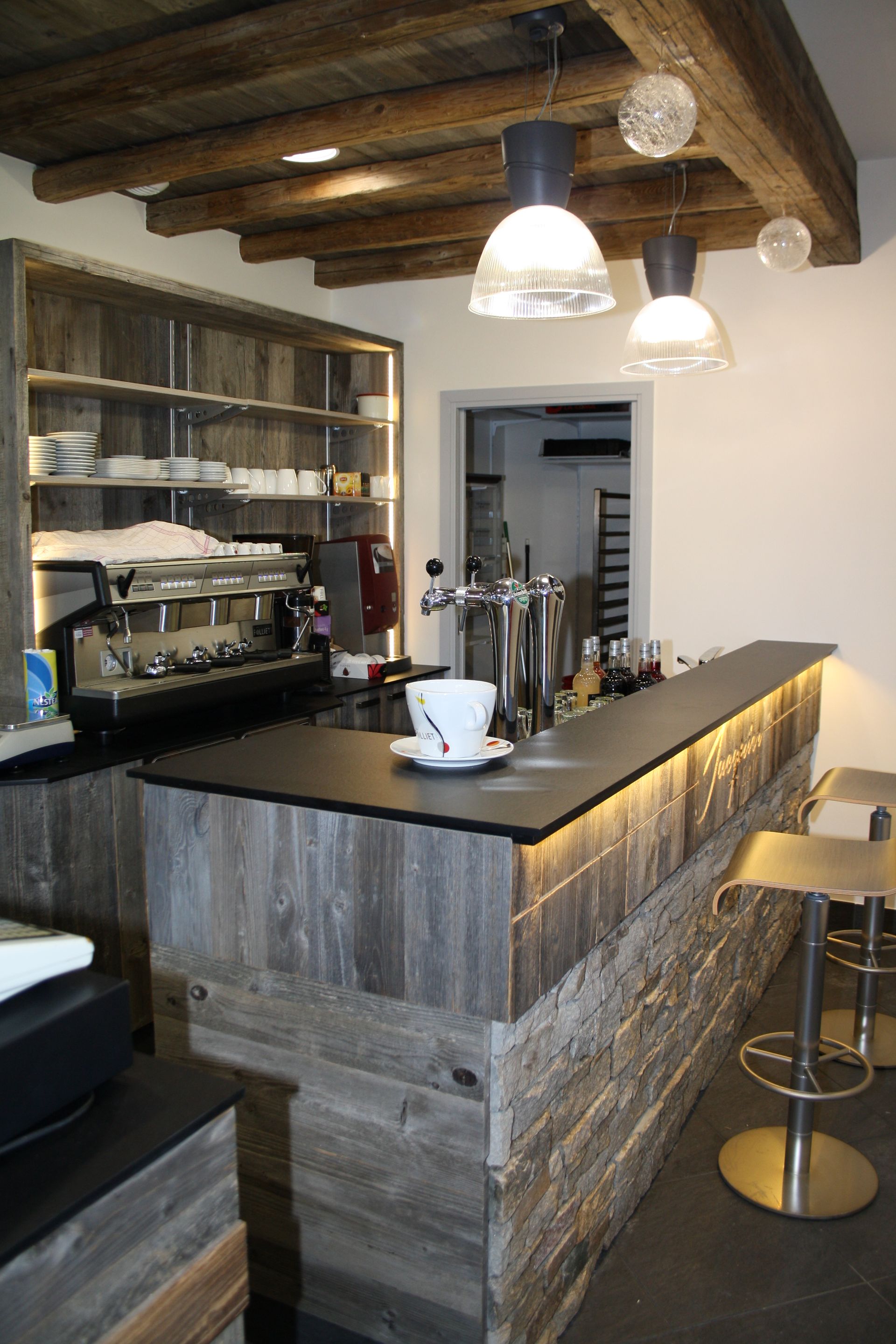 Intérieur de bar rustique avec des éléments en bois, un comptoir avec éclairage intégré et des suspensions lumineuses.