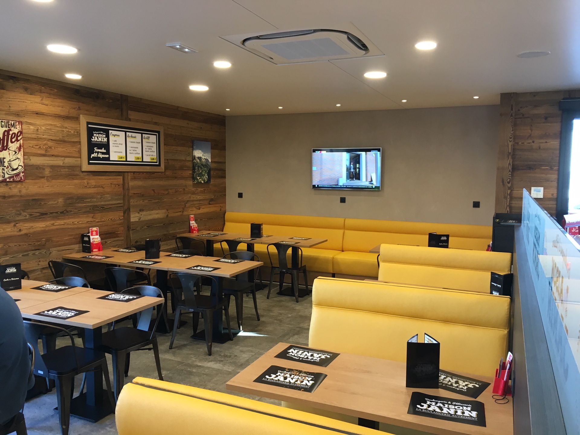 Intérieur d'un restaurant avec des banquettes jaunes, des boiseries, des tables et une télévision au mur.