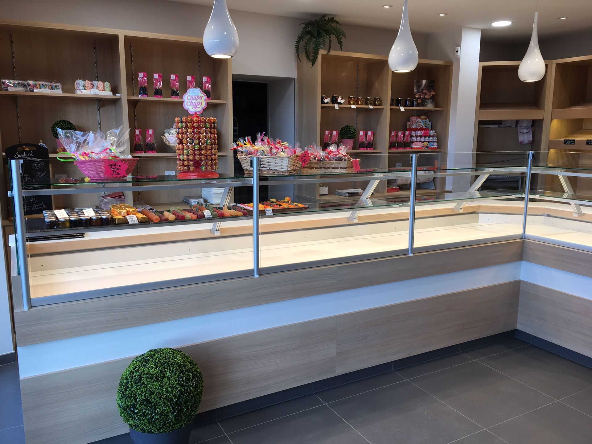 Intérieur de boulangerie avec vitrine à pâtisseries, étagères en bois et éclairage zénithal.