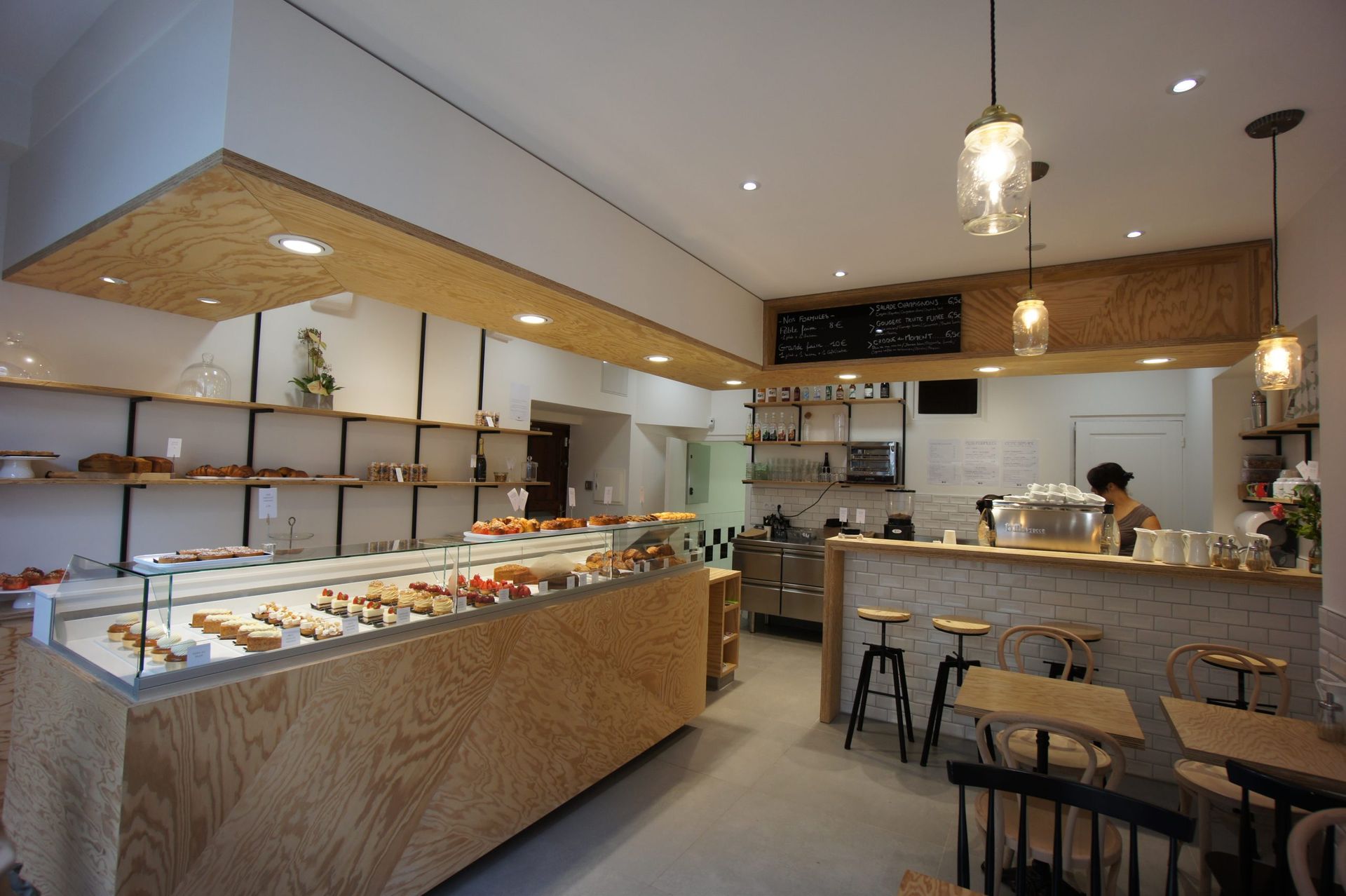 Intérieur d'une boulangerie avec des pâtisseries exposées dans une vitrine et une personne travaillant derrière le comptoir.