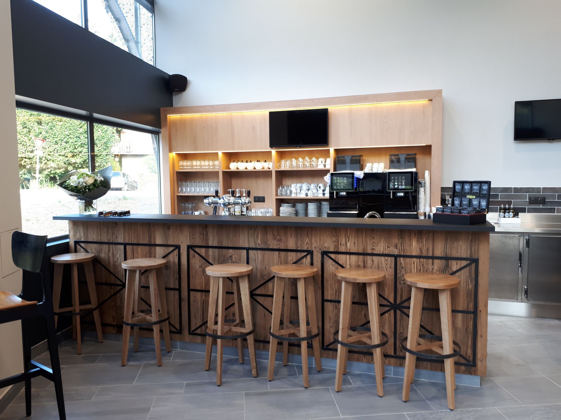 Coin bar avec tabourets et comptoir en bois, verres et machines à café.