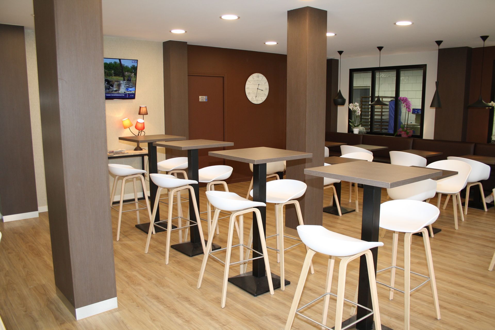 Intérieur d'un café avec des tables carrées, des tabourets blancs et des murs bruns et blancs.