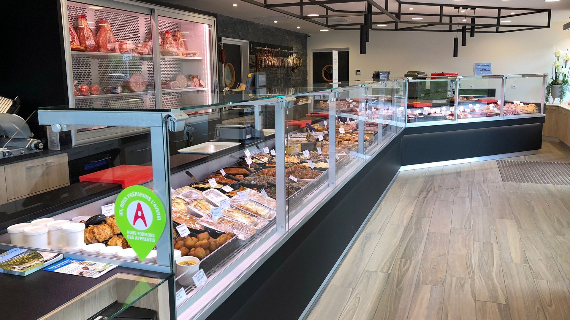 Intérieur d'une boucherie avec vitrines présentant des produits carnés. Sol en bois et éclairage fluorescent.