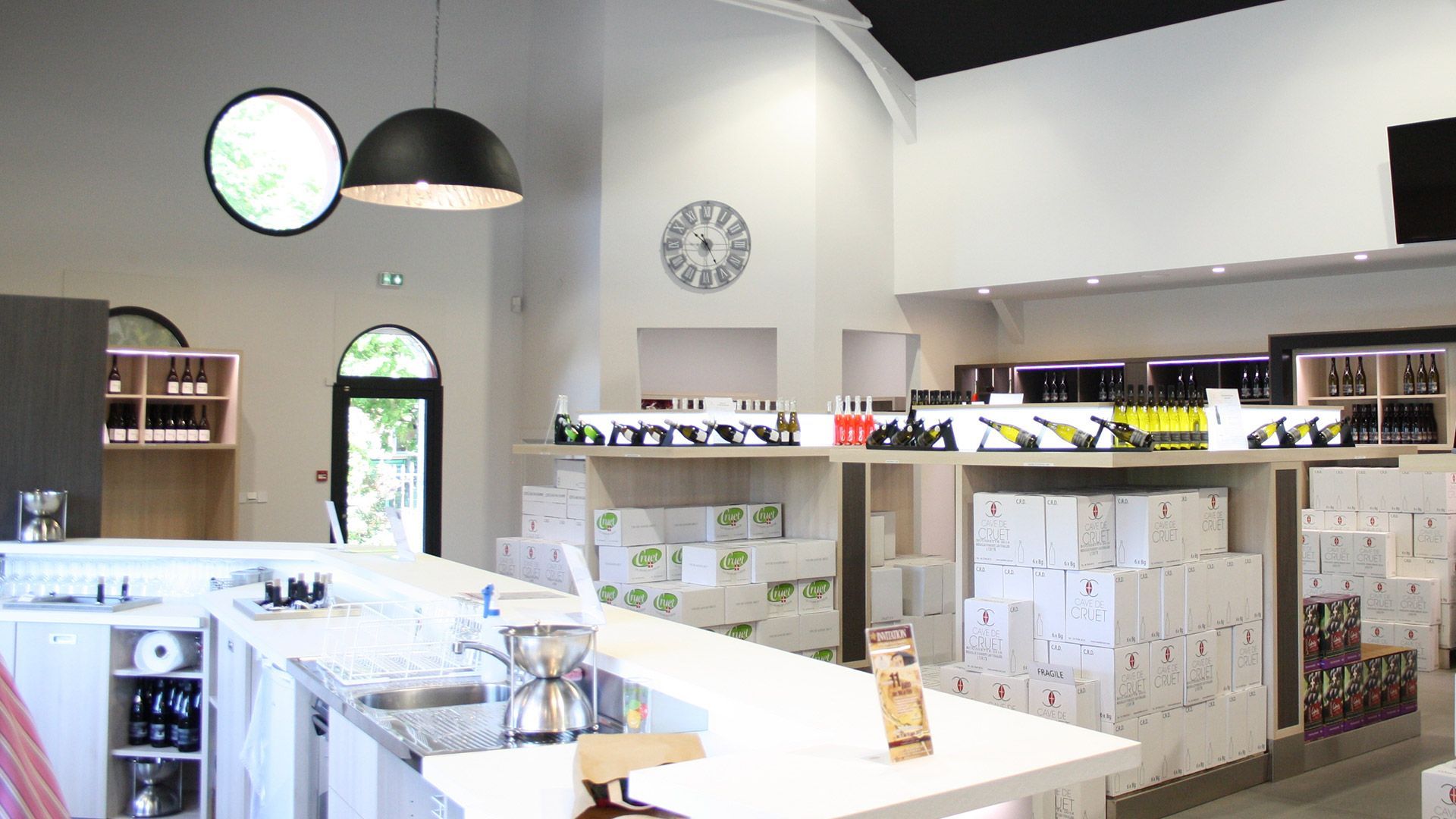 Intérieur lumineux d'une cave à vin avec un bar blanc et des présentoirs de caisses et de bouteilles.