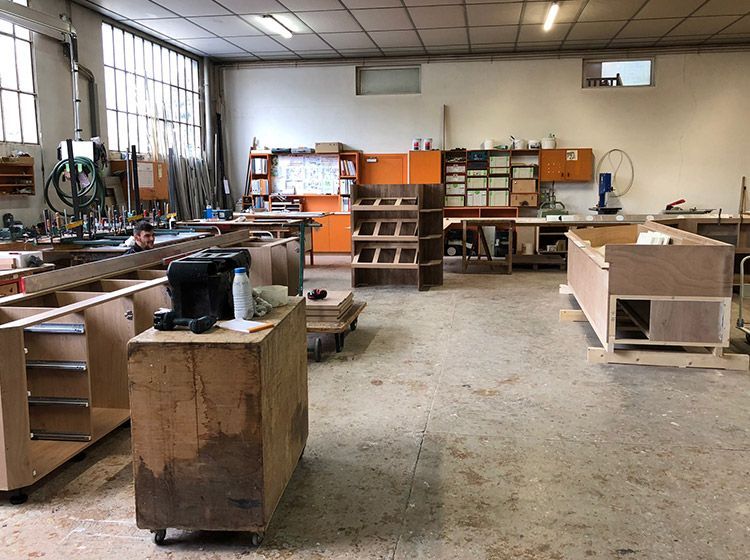 Intérieur d'atelier avec des éléments de mobilier en bois à différents stades de construction ; lumineux et encombré.