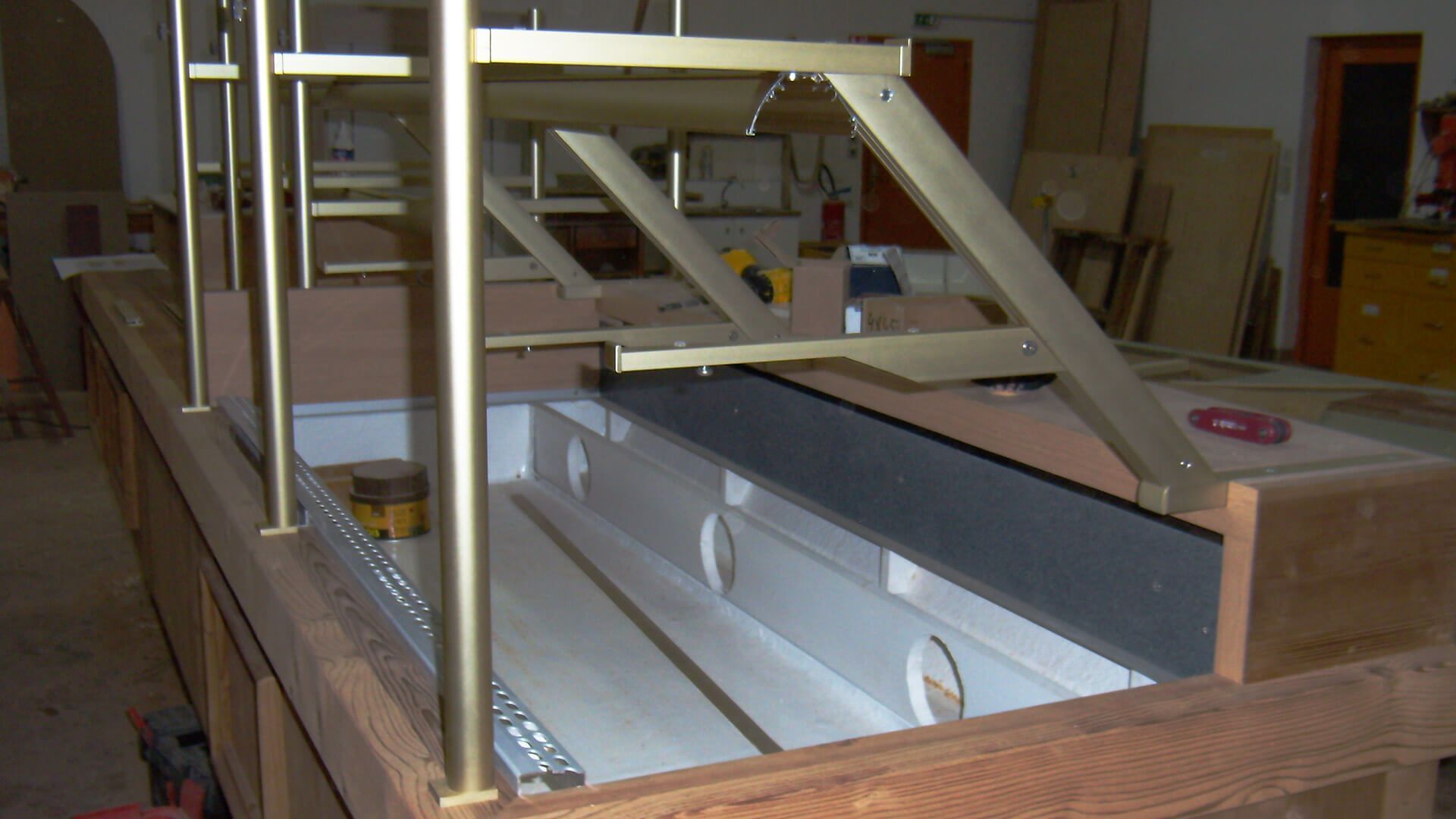 Structure à armature en laiton surmontant un meuble en bois avec une longue partie intérieure ouverte.