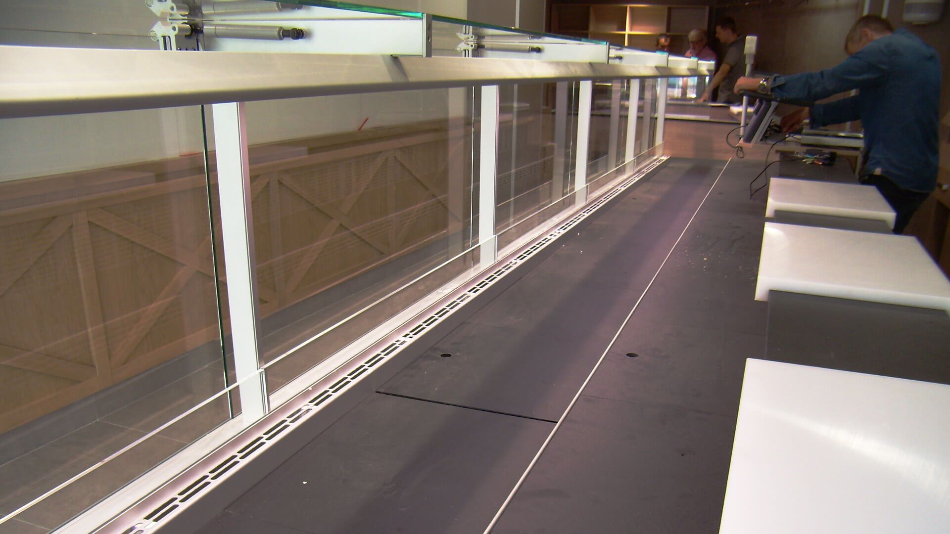 Un homme travaille sur une longue vitre. Cadre blanc, surface sombre, environnement industriel.