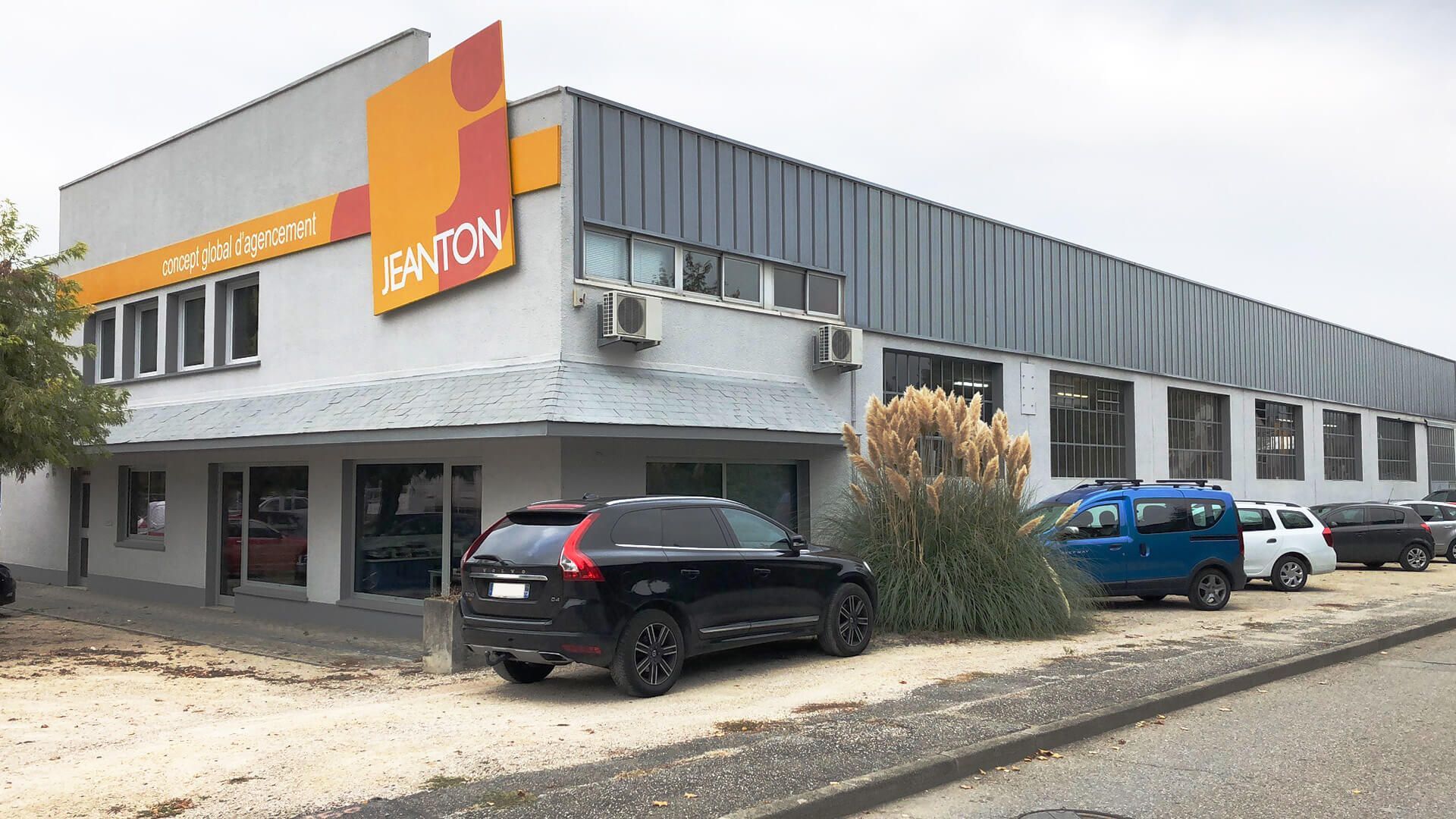 Un bâtiment industriel moderne. Des voitures sont garées devant.