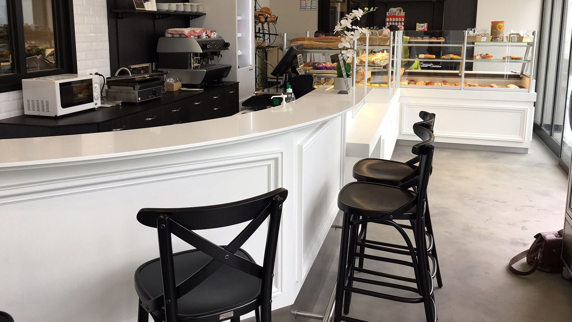 Intérieur du café : comptoir blanc avec tabourets, présentoir de pâtisseries, décor noir et blanc.