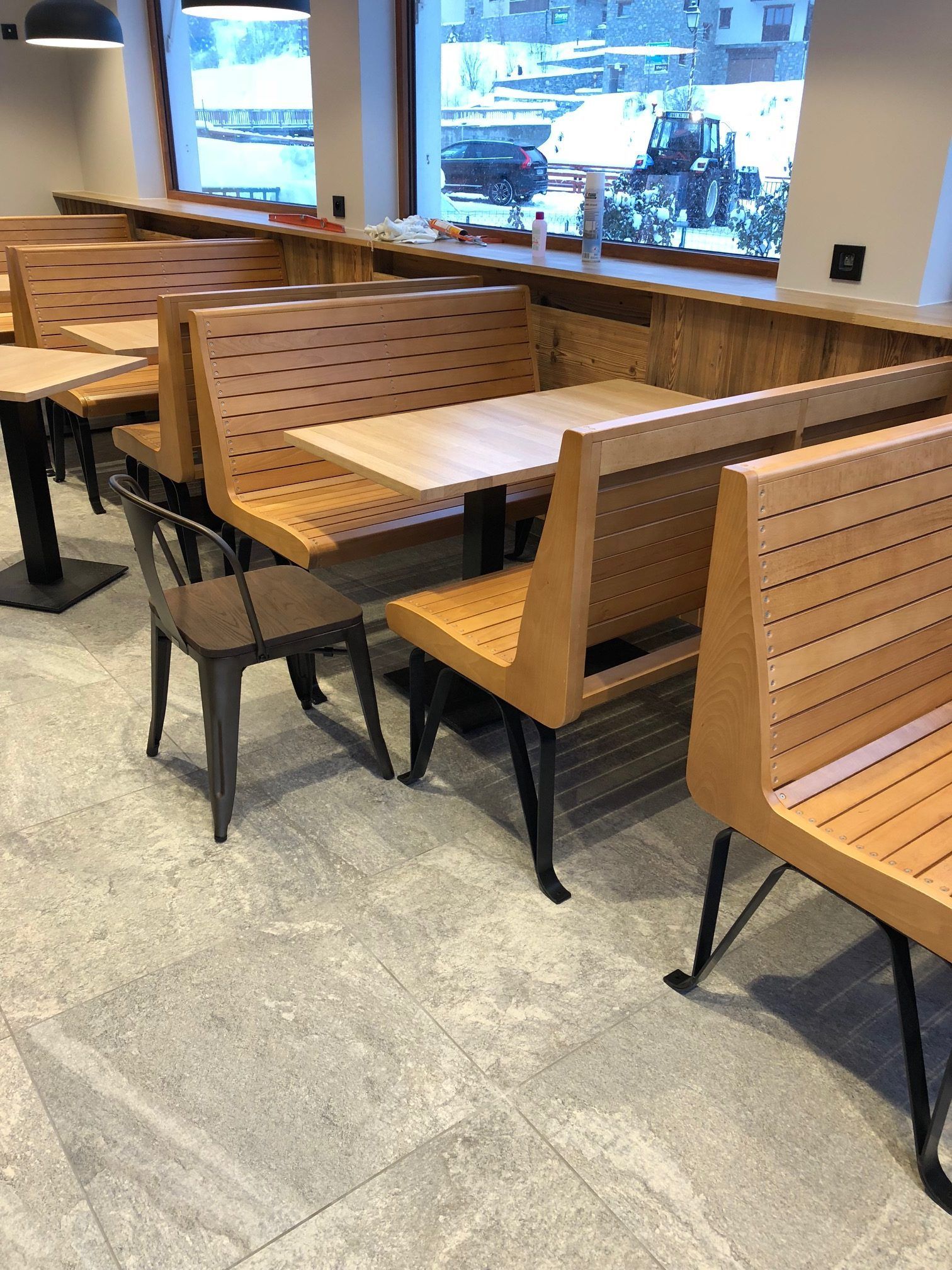 Des banquettes en bois et une chaise en métal sont disposées dans un restaurant, près d'une fenêtre.