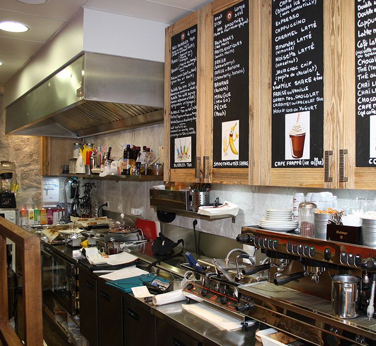 Intérieur de la cuisine d'un café : comptoirs en acier inoxydable, panneaux de menus, machine à expresso et hotte aspirante.