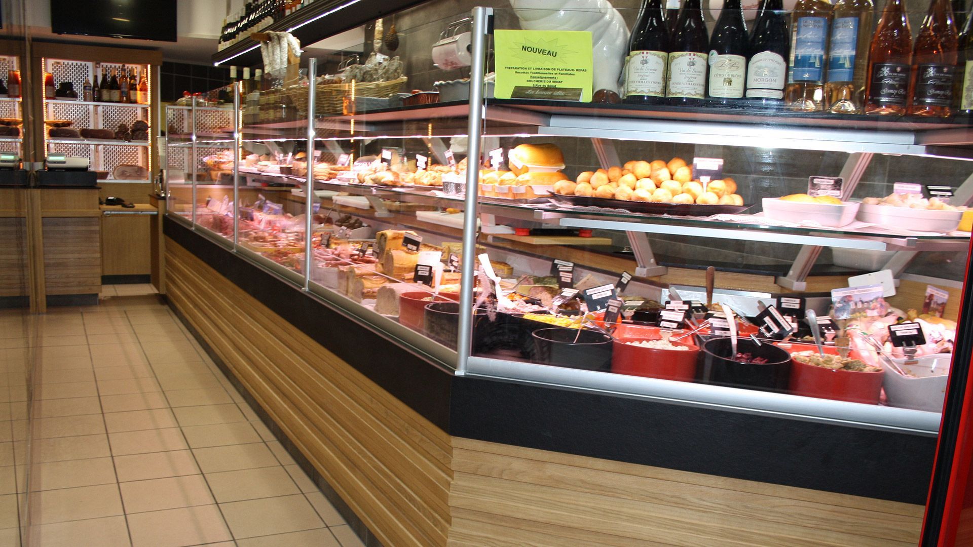 Une vitrine de charcuterie remplie de plats préparés. Des bouteilles de vin sont visibles en arrière-plan.