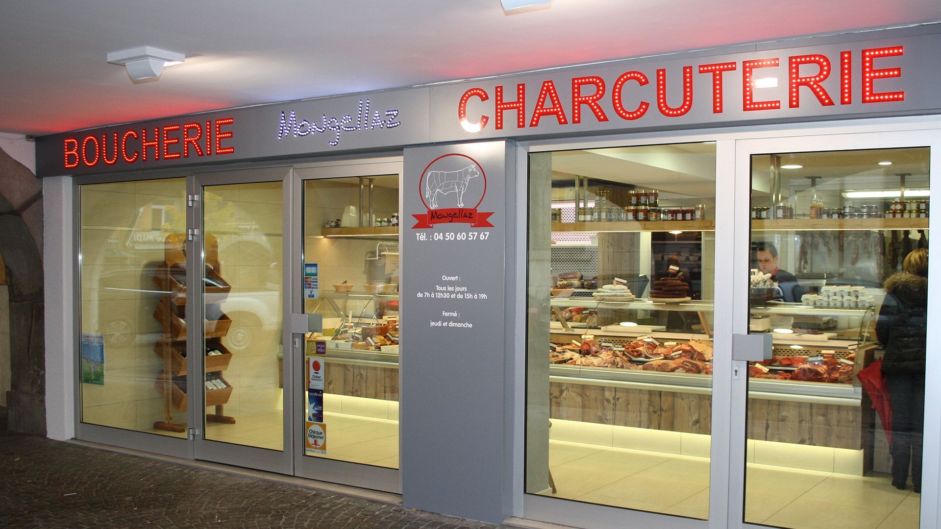 Façade de boucherie avec étalage de viandes ; enseigne rouge « CHARCUTERIE ».