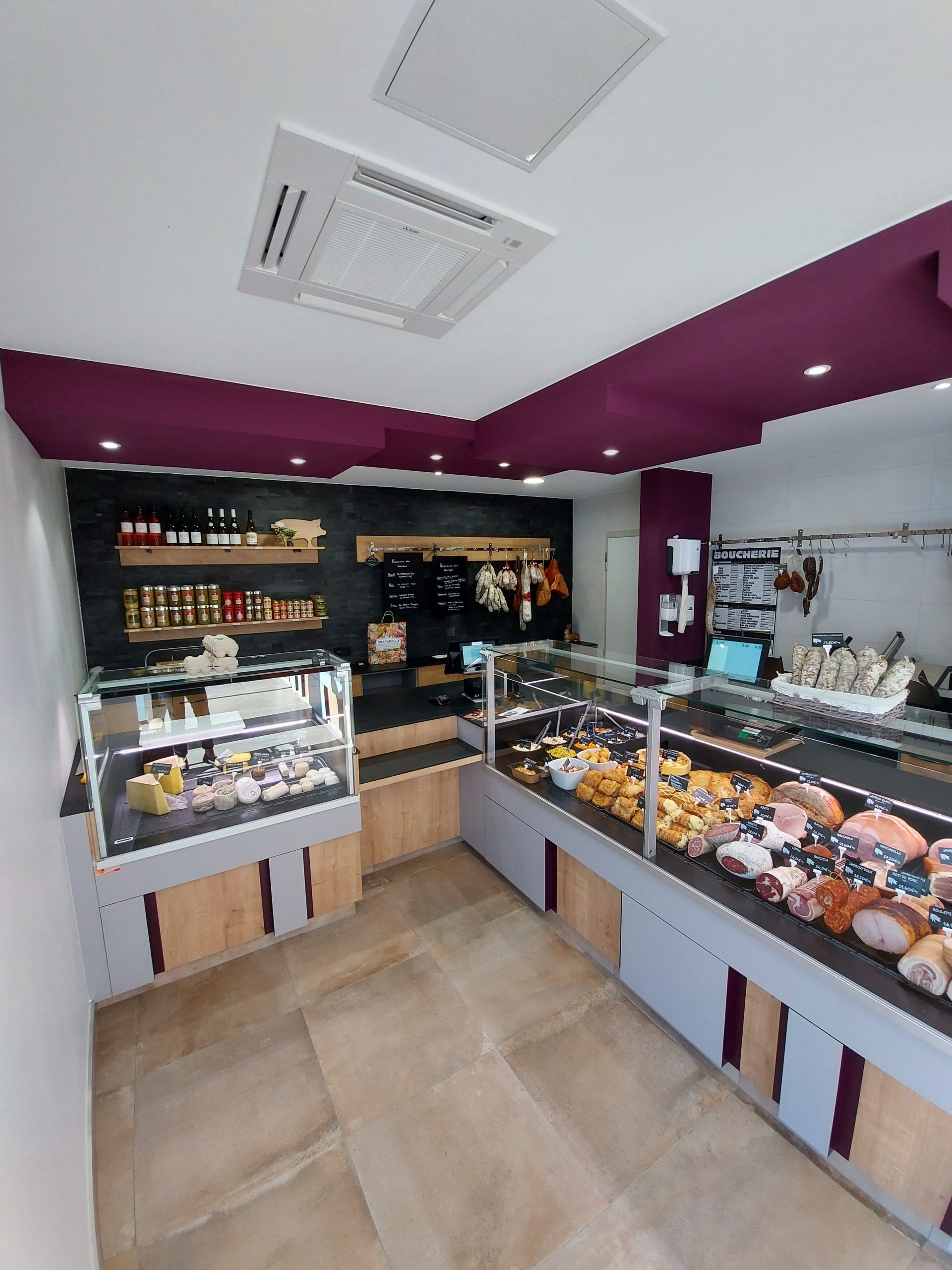 Intérieur d'une épicerie fine avec vitrines de produits alimentaires. Plafond bordeaux, éléments en bois clair et divers plats préparés.