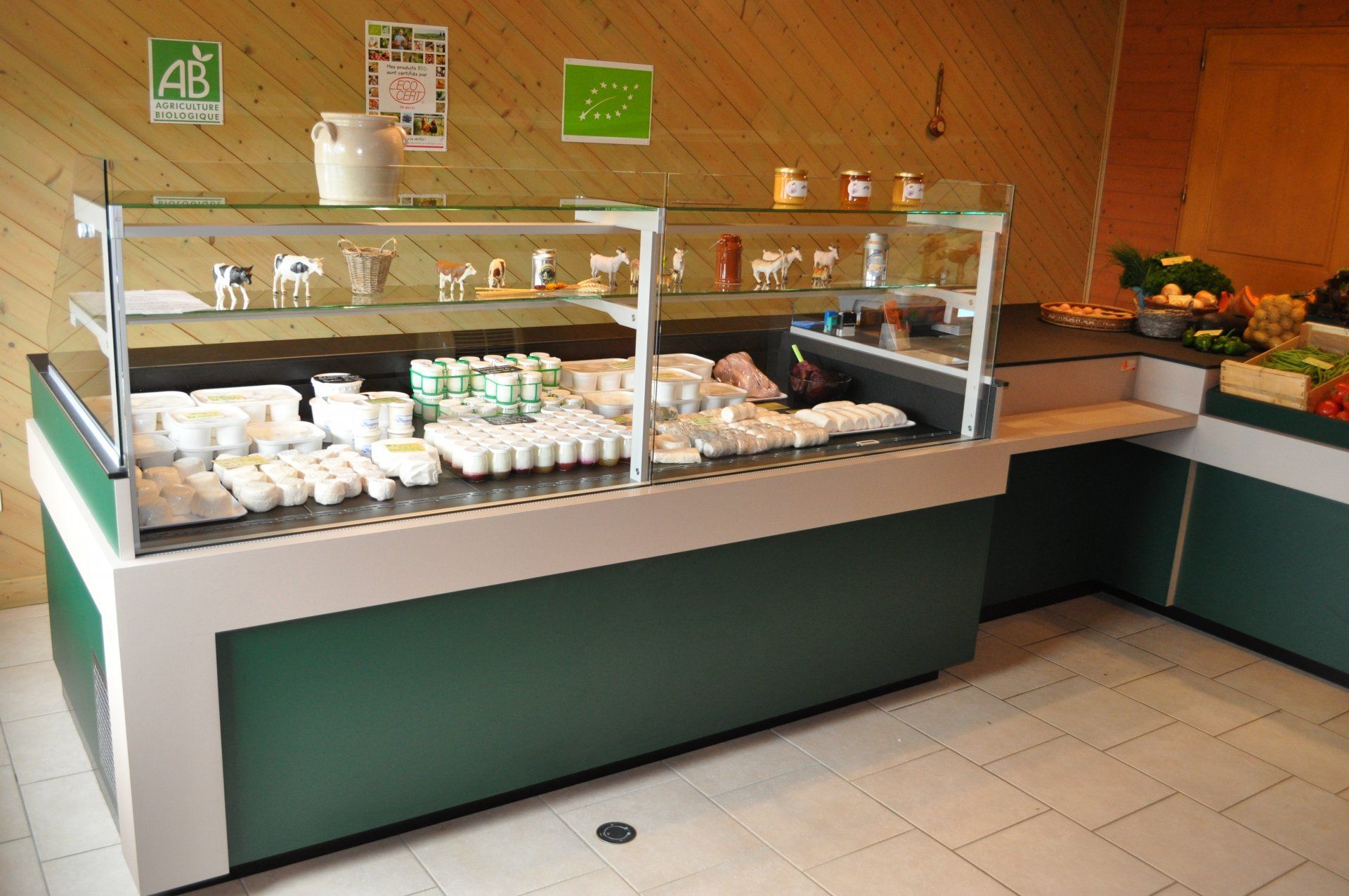 Vitrine remplie de produits laitiers dans un magasin, avec des figurines décoratives de vaches sur une étagère supérieure.