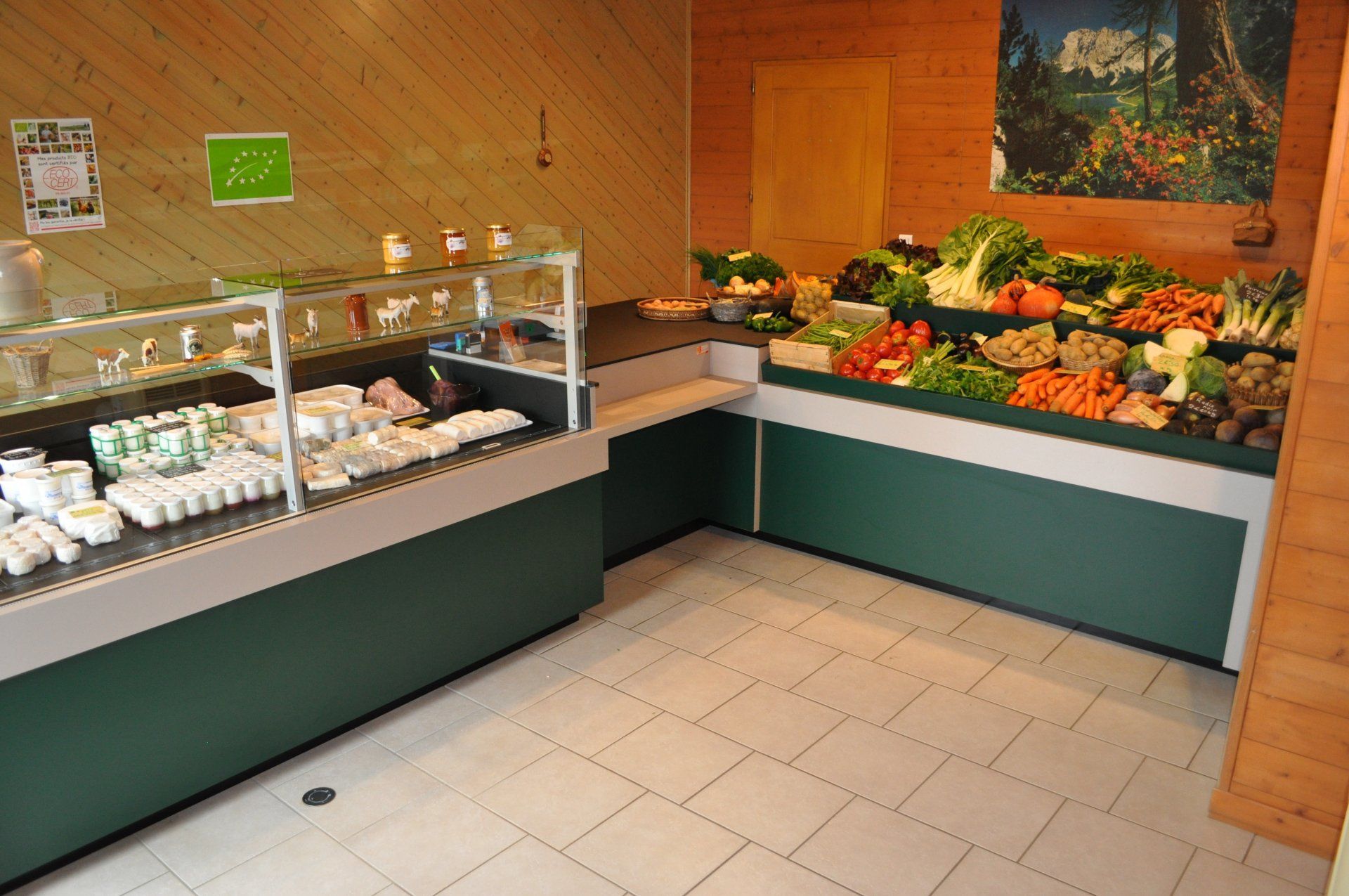 Intérieur d'une petite épicerie avec des comptoirs verts présentant des produits laitiers et des fruits et légumes frais.