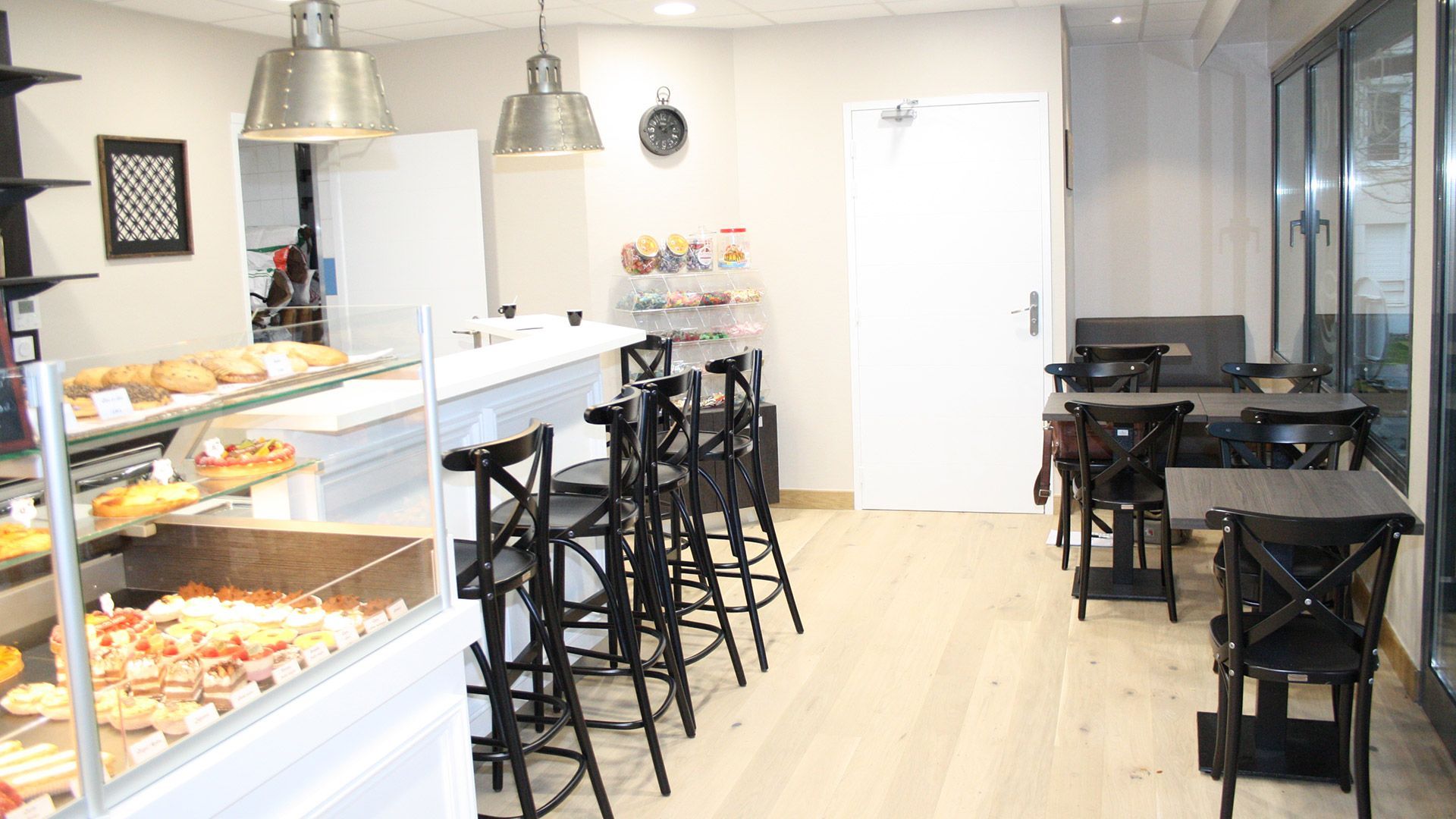Intérieur de la boulangerie avec vitrine à pâtisseries, comptoir et petites tables.