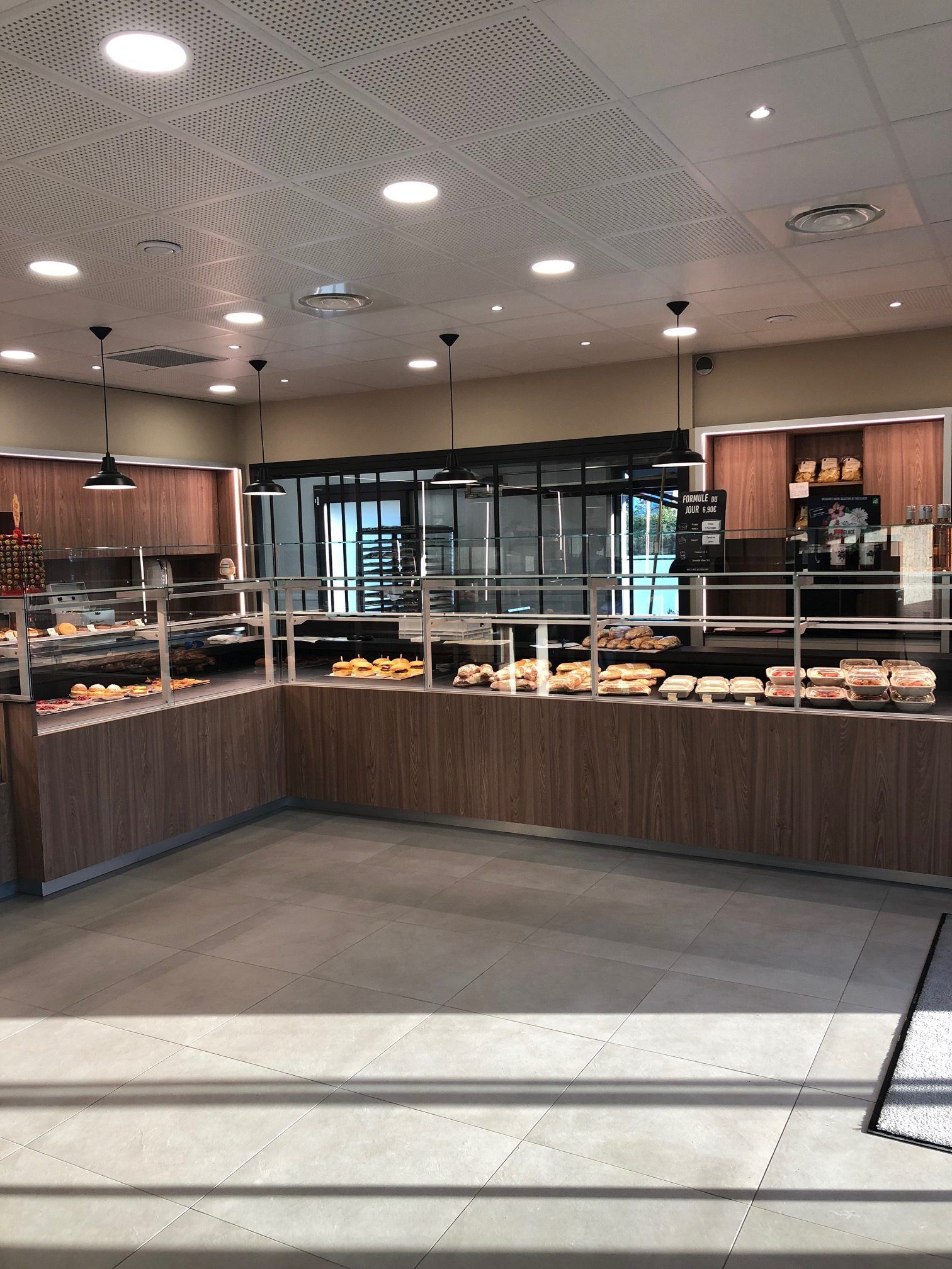 Vue intérieure d'une boulangerie avec des vitrines remplies de pâtisseries, des comptoirs en bois et un éclairage encastré.