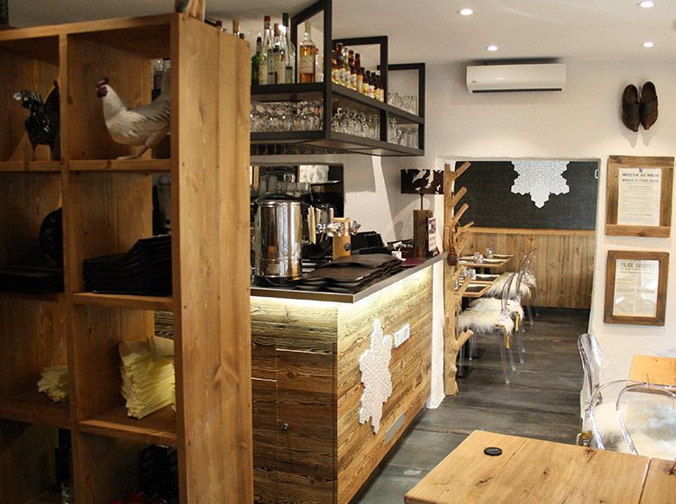 Intérieur d'un restaurant avec décor en bois, bar et sièges. Murs blancs.