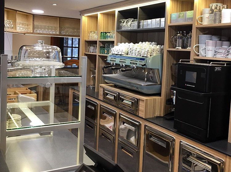 Comptoir de café avec machine à expresso, étagères et vitrine.