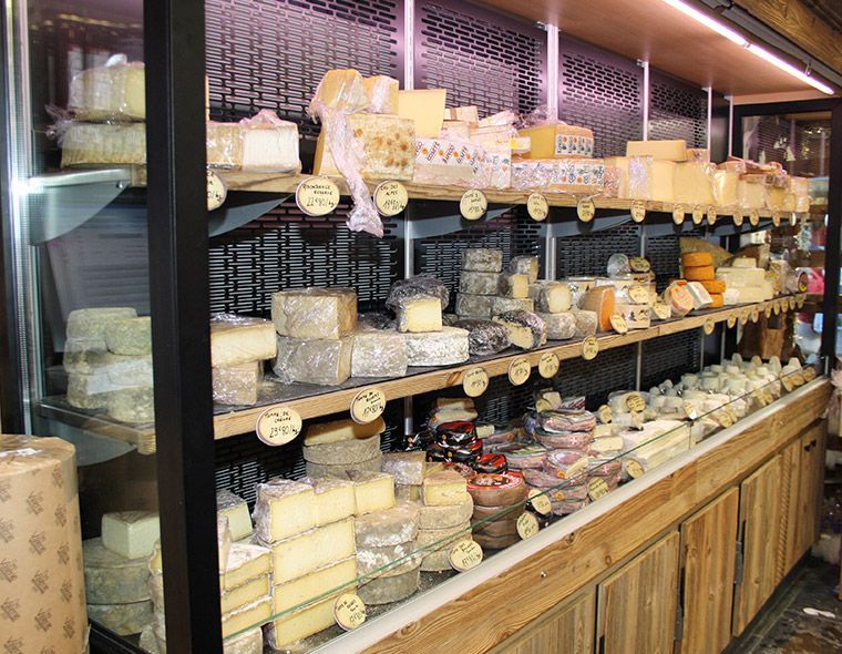 Présentoir à fromages dans un magasin, étagères en bois, différents types de fromages, certains étiquetés avec les prix.