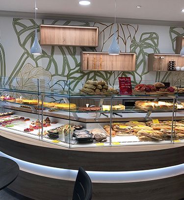 Vitrine de boulangerie présentant diverses pâtisseries. L'intérieur est agrémenté d'éléments en bois et d'un décor mural à motifs botaniques.