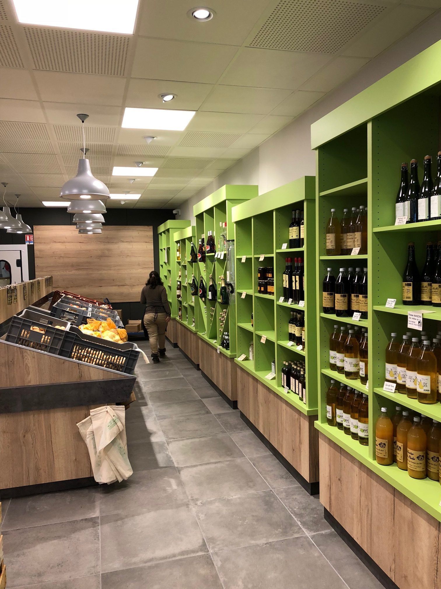 Intérieur d'un supermarché : rayons de produits en bouteille, étalage de fruits et légumes, client faisant ses courses.