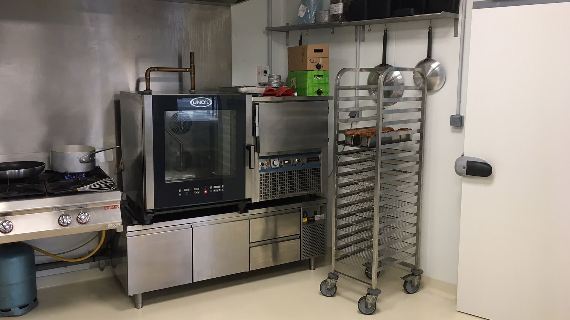 Cuisine professionnelle équipée d'un four, d'une cuisinière et d'un chariot roulant.