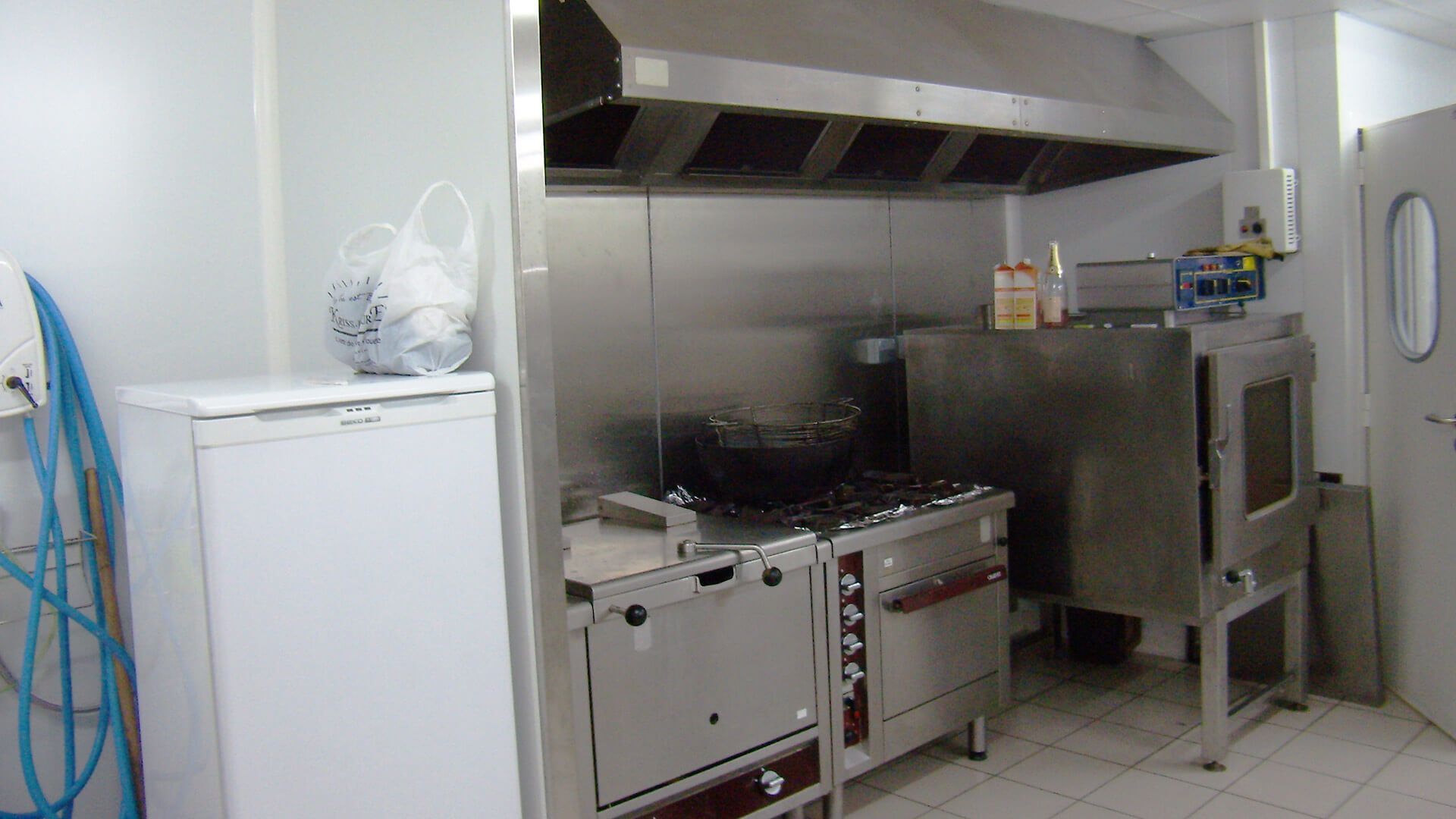 Cuisine commerciale équipée d'appareils en acier inoxydable, cuisinière, four et hotte aspirante.